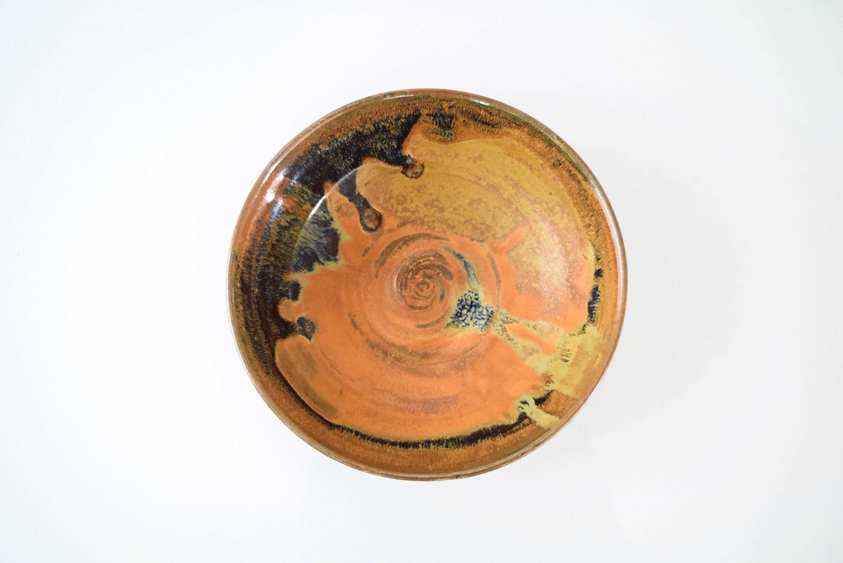This vintage Mid-Century Modern ceramic pottery bowl is circa 1960. It features a simple modernist handcrafted design with beautiful shades of natural burnt orange, gold, blue and black in varying sheens.

Dimensions:
Diameter 7 1/8