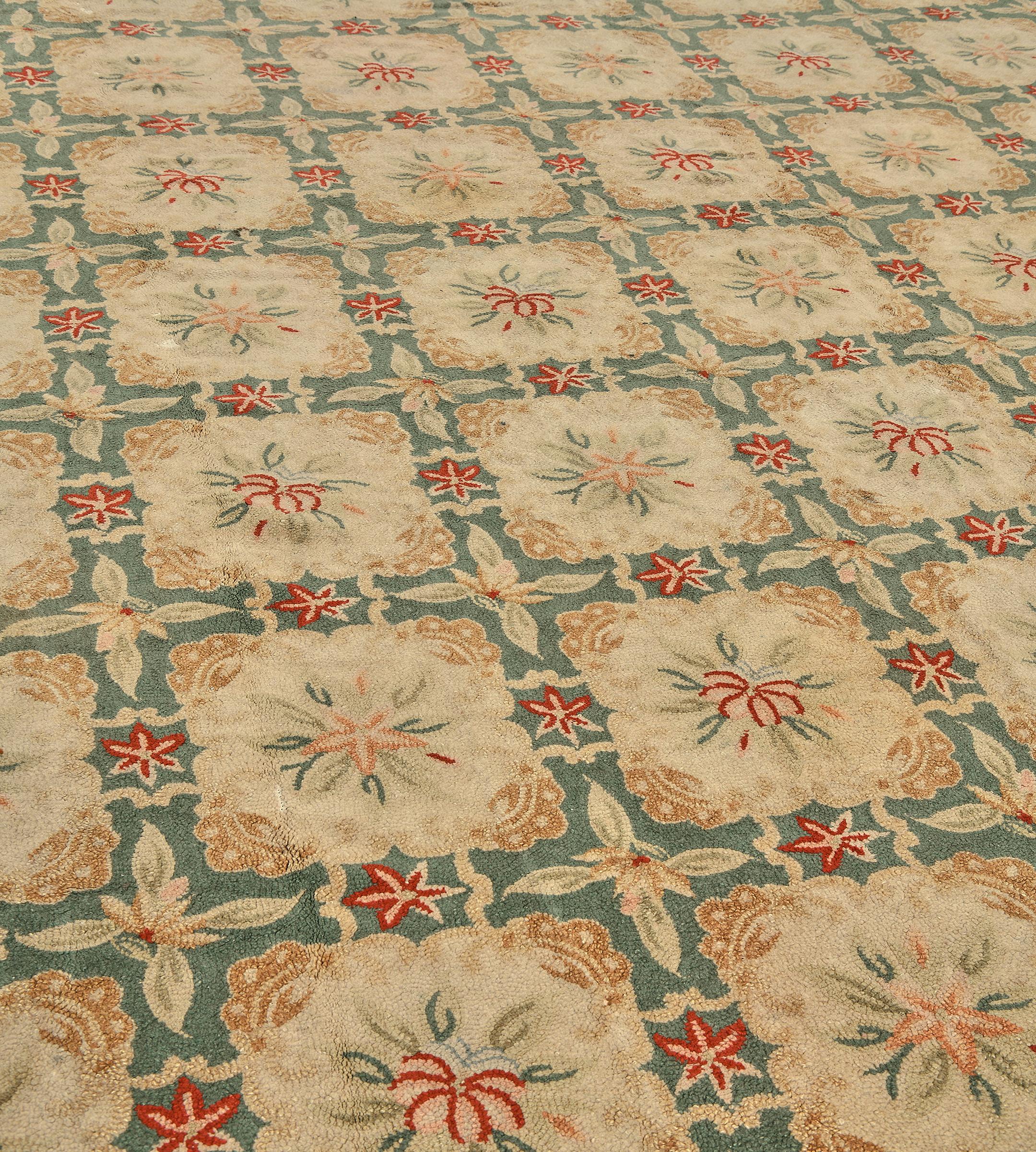This vintage American Hooked floral rug features a sea-green field with seven columns of ten ivory square shaped panels with a central inner floral spray and each square panel surrounded by a large floral motif at each corner and a tomato-red and