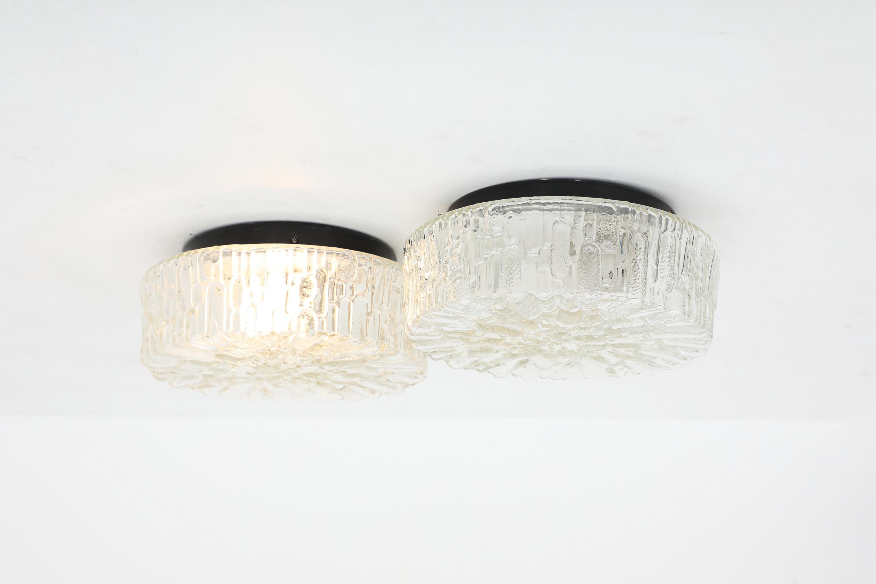 Gorgeous heavy round molded glass ceiling or wall sconces with Brutalist embossed design. In original condition with visible wear consistent with its age and use. This lamp is hardwired and takes a medium base E26/E27 bulb. Two available. Sold