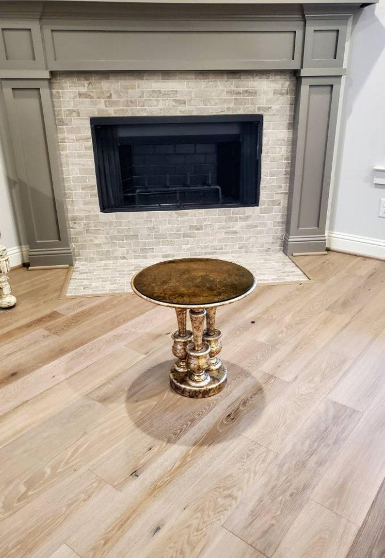 A stunning and unusual mid-century gilt occasional table featuring a circular dish shaped top with inset smoked glass topper, over three tapered turned vasiform bulbous shaped footed ringed base columns, rising on circular base. Richly embellished
