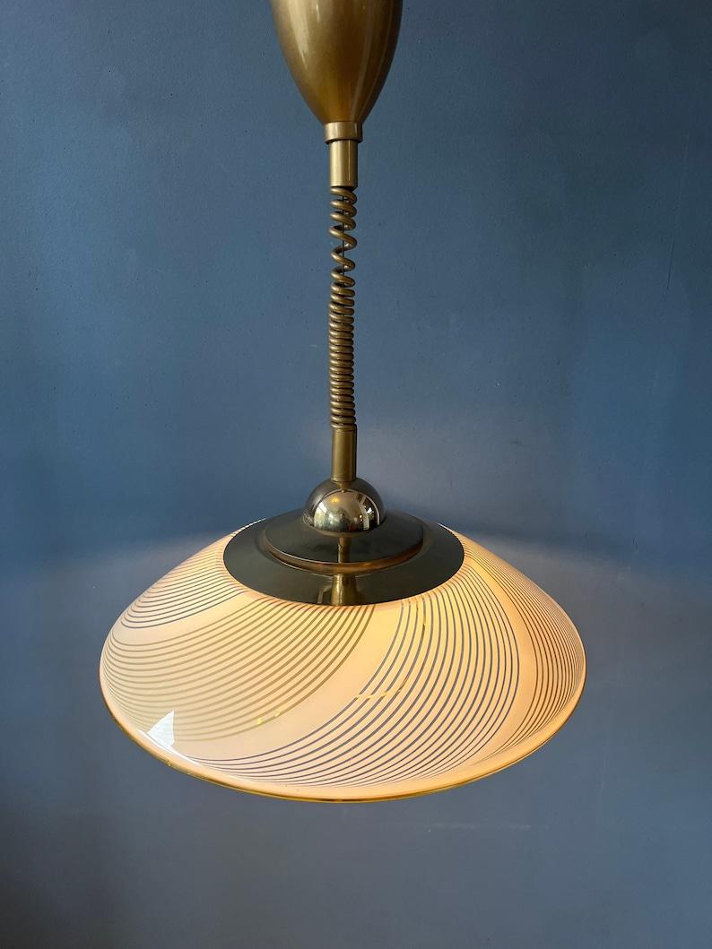Lampe suspendue vintage mid century Hollywood regency avec abat-jour clair et éléments dorés. L'abat-jour en verre acrylique produit une lumière agréable. La hauteur peut être facilement réglée grâce au mécanisme de montée et de descente. La lampe