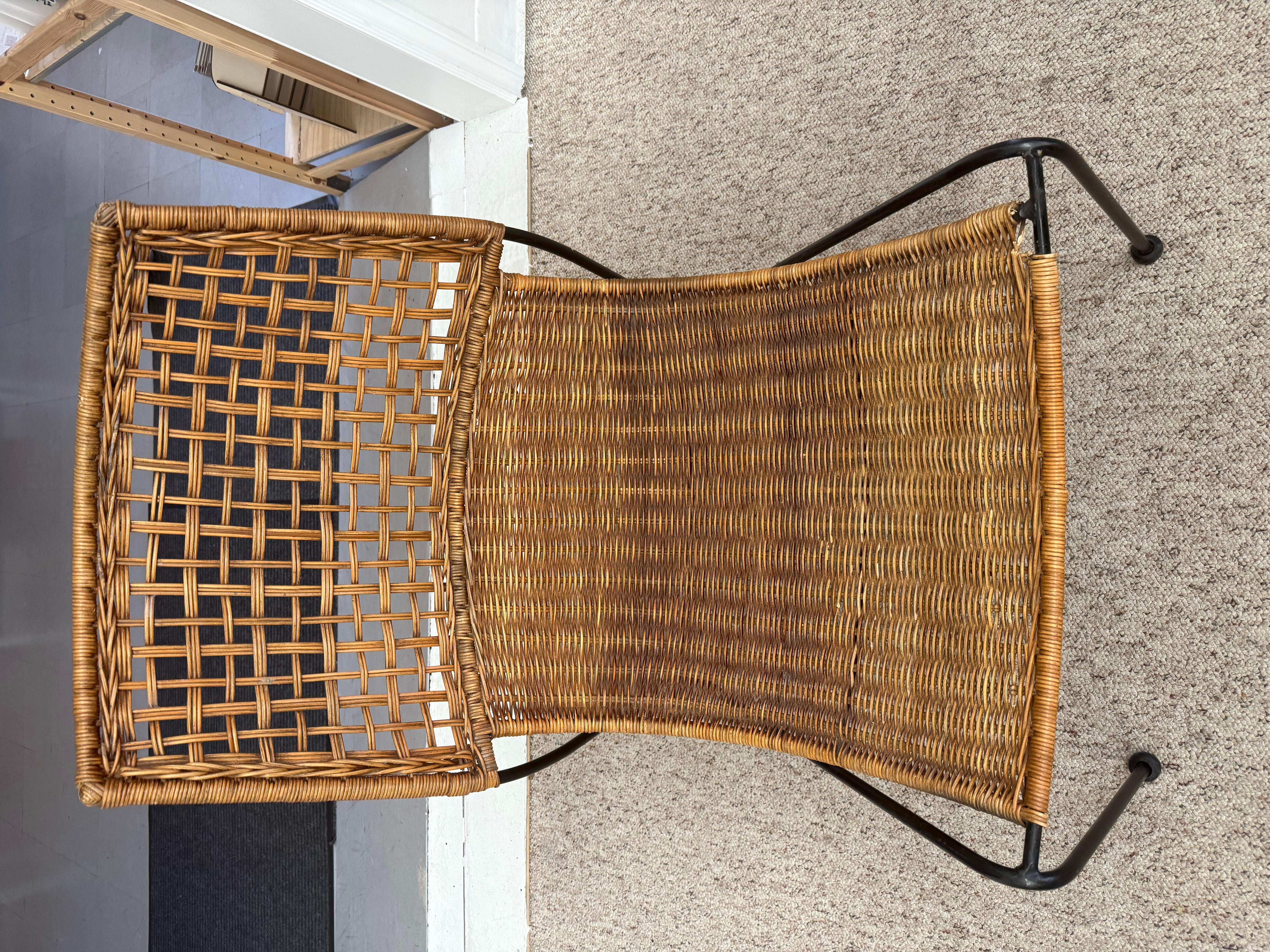 The Vintage Mid Century Modern Iron and Wicker Sling Chair attributed to Frederick Weinberg features a distinctive design characteristic of the mid-20th century. The chair has a sleek, minimalist frame made of black iron, which provides a sturdy and