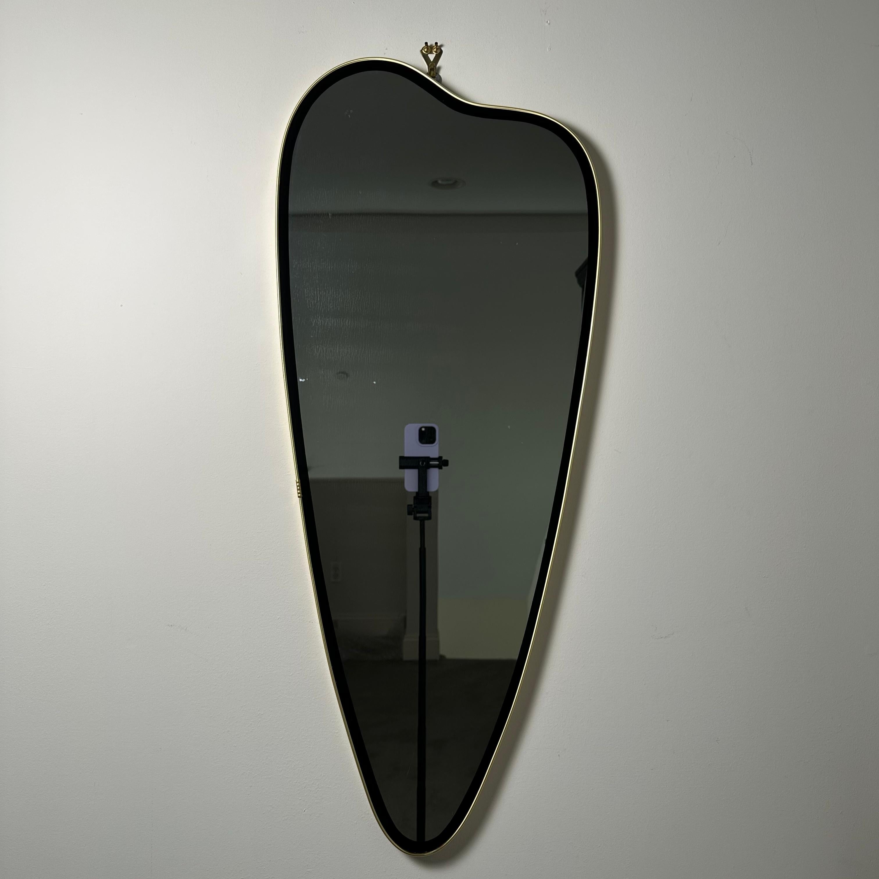 Vintage Italian Mid-Century Modern hanging wall mirror framed in brass with black reverse painted glass border. This mirror is quite large and has a freeform organic shape inspired by a painter's palette. Currently fitted with 2 hardware options for