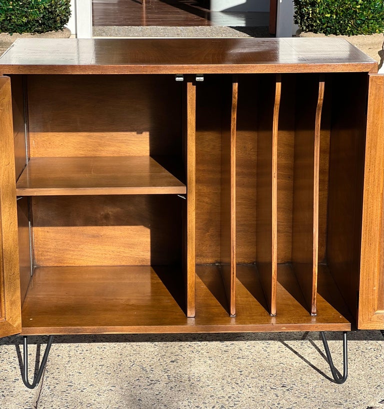 Gorgeous 1960's John Stuart walnut server on hairpin legs. Cabinetry is comprised of four tray dividers and two shelves providing ample space and organization for serving pieces. Doors open and close easily with a push mechanism which clicks into