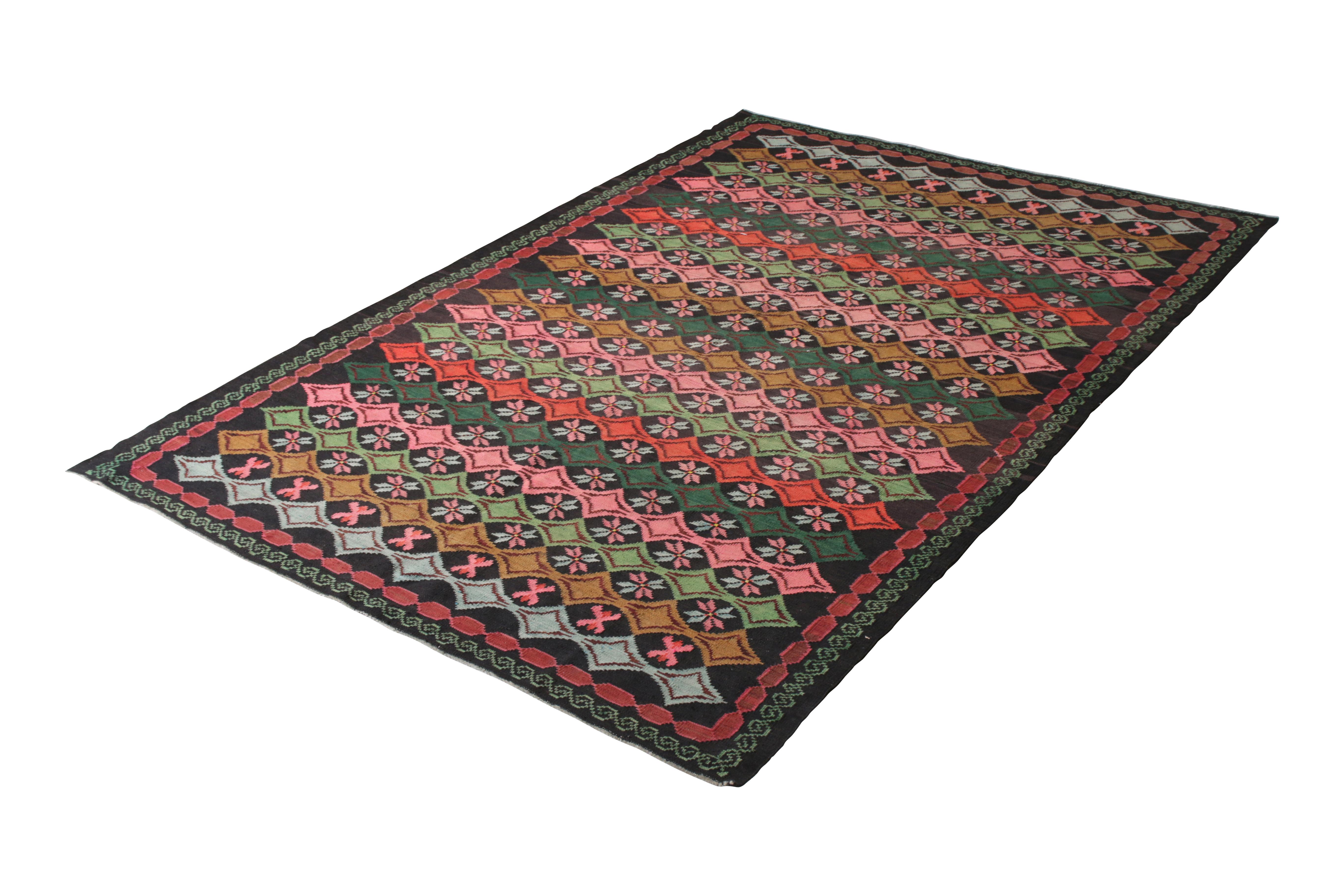 Handwoven in a wool flat-weave originating from Turkey, circa 1950-1960, this vintage Kilim rug connotes a midcentury Turkish Kilim rug design in a notably unique colorway, enjoying an uncommon play of rich forest green with accenting hues of pink,
