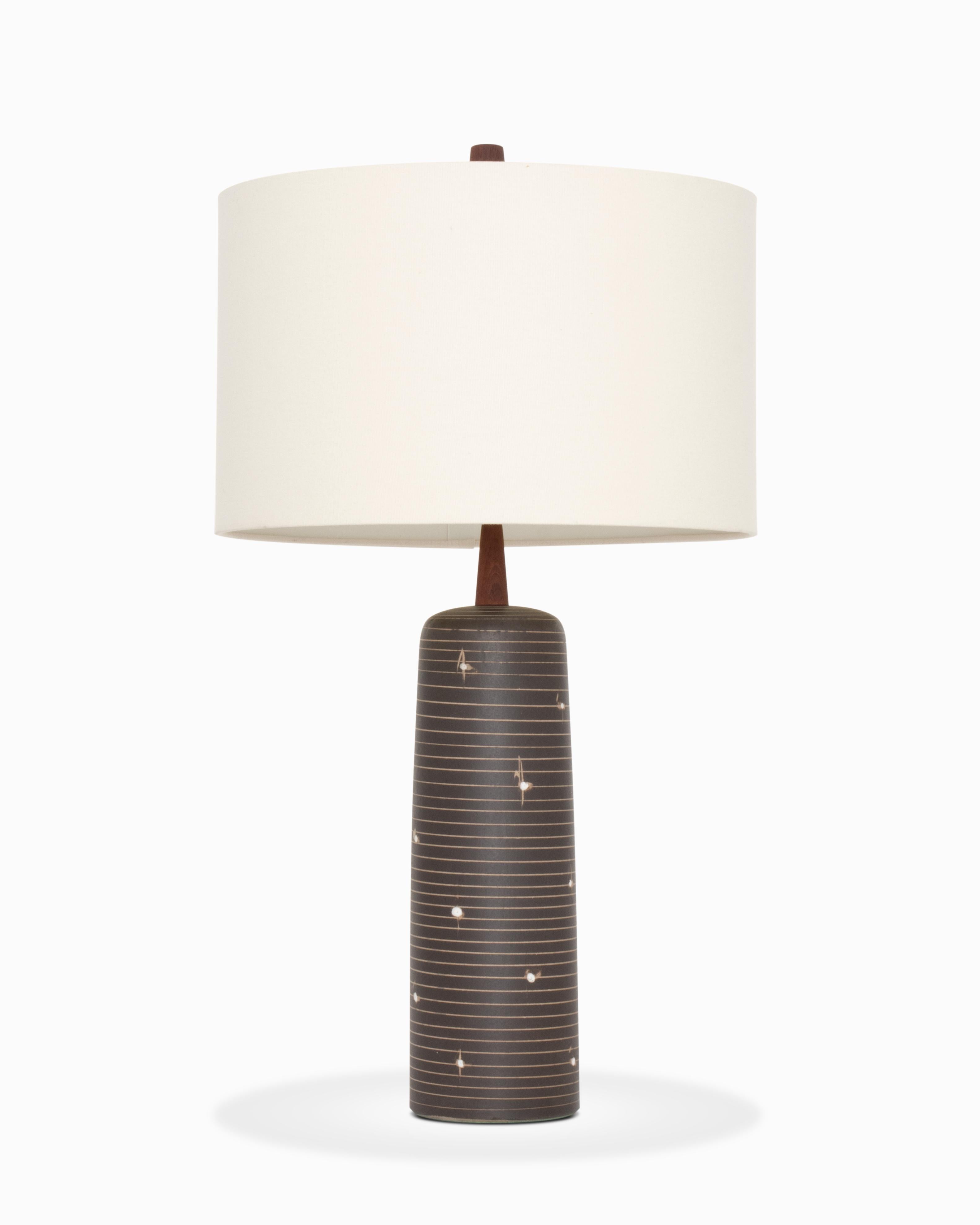 Voici une magnifique lampe de table en céramique de Jane et Gordon Martz / Marshall Studios.  Le modèle 41 présente une forme cylindrique avec des accents en noyer.  La couleur est noire mate avec des incisions de couleur beige et des décorations