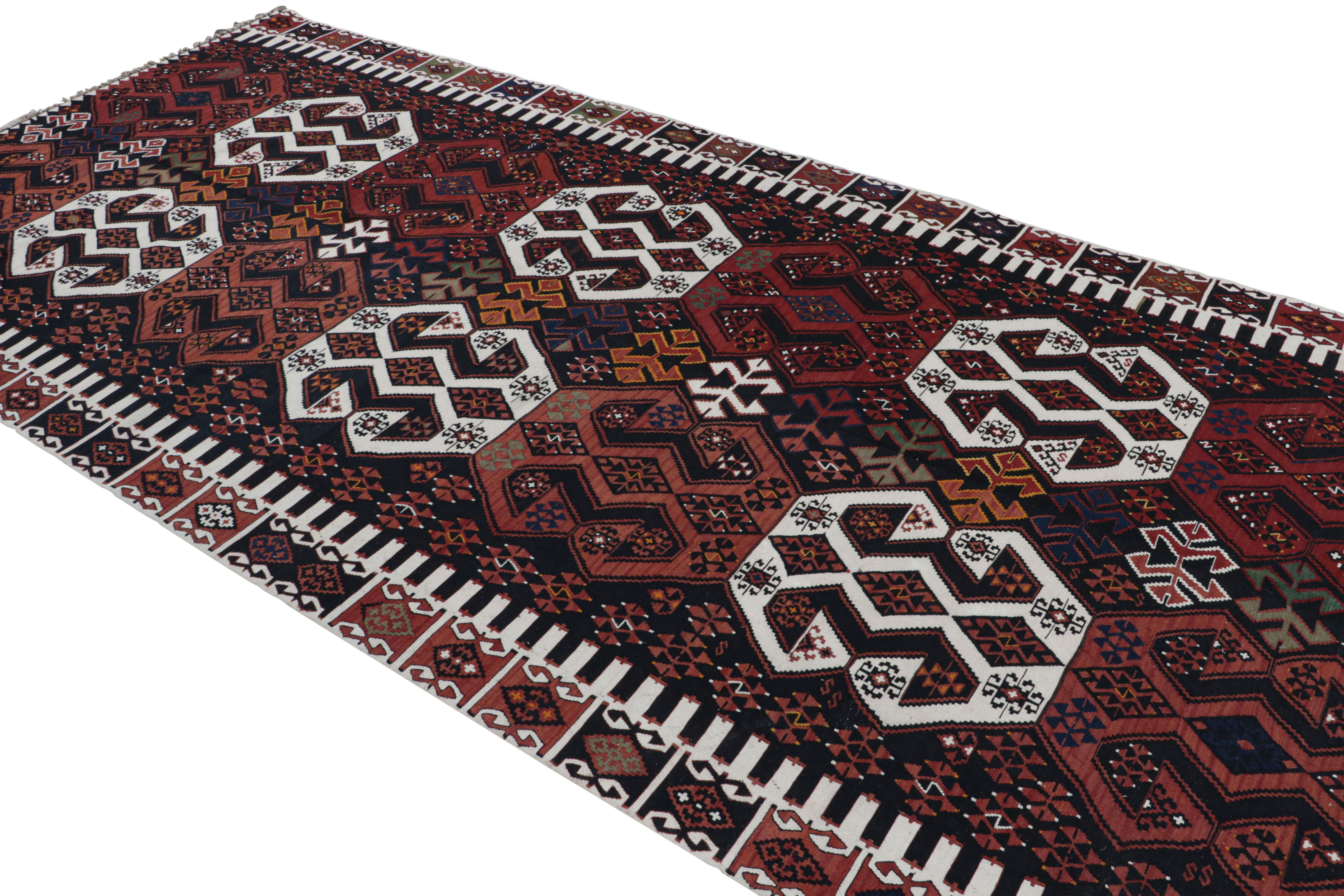 Flat-woven in Turkey originating between 1950-1960, this vintage midcentury geometric Kilim hails from the city of Malatya, enjoying a bold tribal contrast of its rich burgundy red and brown hues with the crisp off-white tones in the colorway,