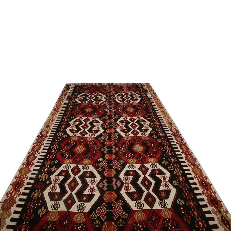 Flat-woven in Turkey originating between 1950-1960, this vintage midcentury geometric Kilim hails from the city of Malatya, enjoying a bold tribal contrast of its rich burgundy red and brown hues with the crisp off-white and soothing yellow tones