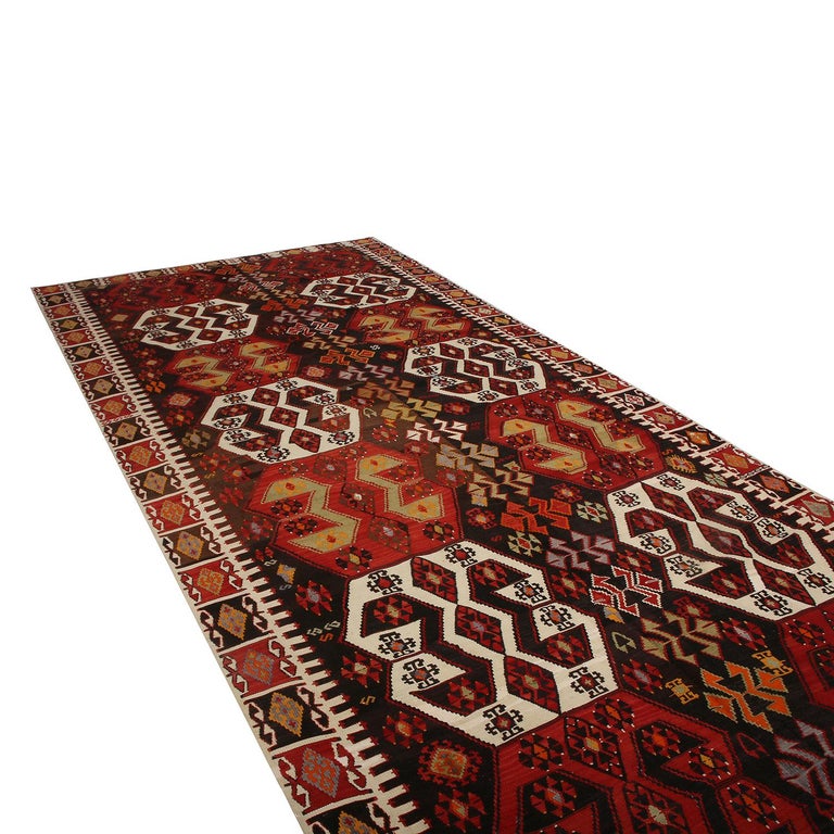 Flat-woven in Turkey originating between 1950-1960, this vintage midcentury geometric Kilim hails from the city of Malatya, enjoying a bold tribal contrast of its rich burgundy red and brown hues with the crisp off-white and soothing green tones
