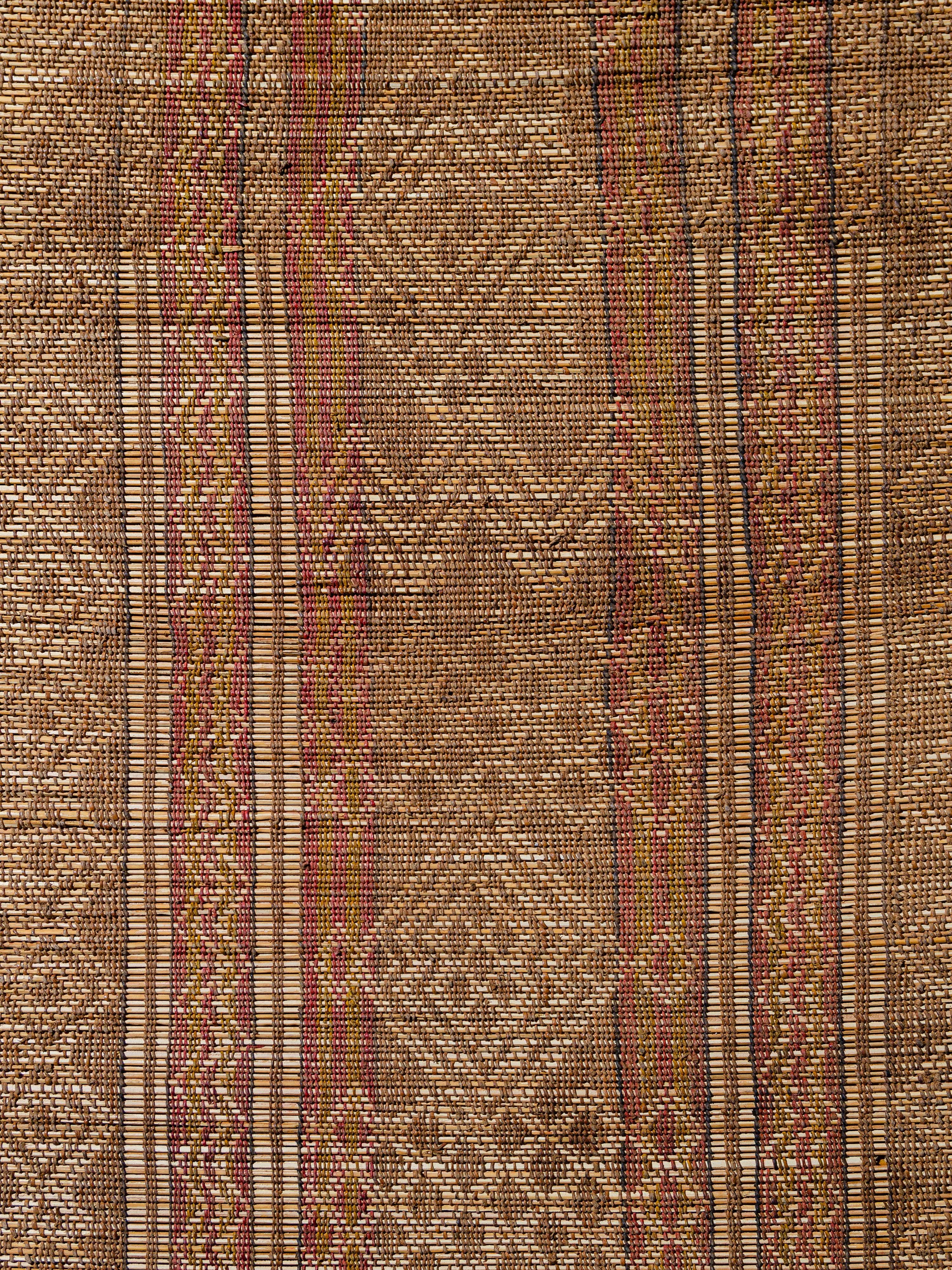 Woven by the nomadic Tuareg tribes of Mauritania with palm reed and camel leather, Tuareg mats offer an alternative to a traditional woven textile floor coverings. This example features vertical bands of intricate motifs, with lozenges, meandering