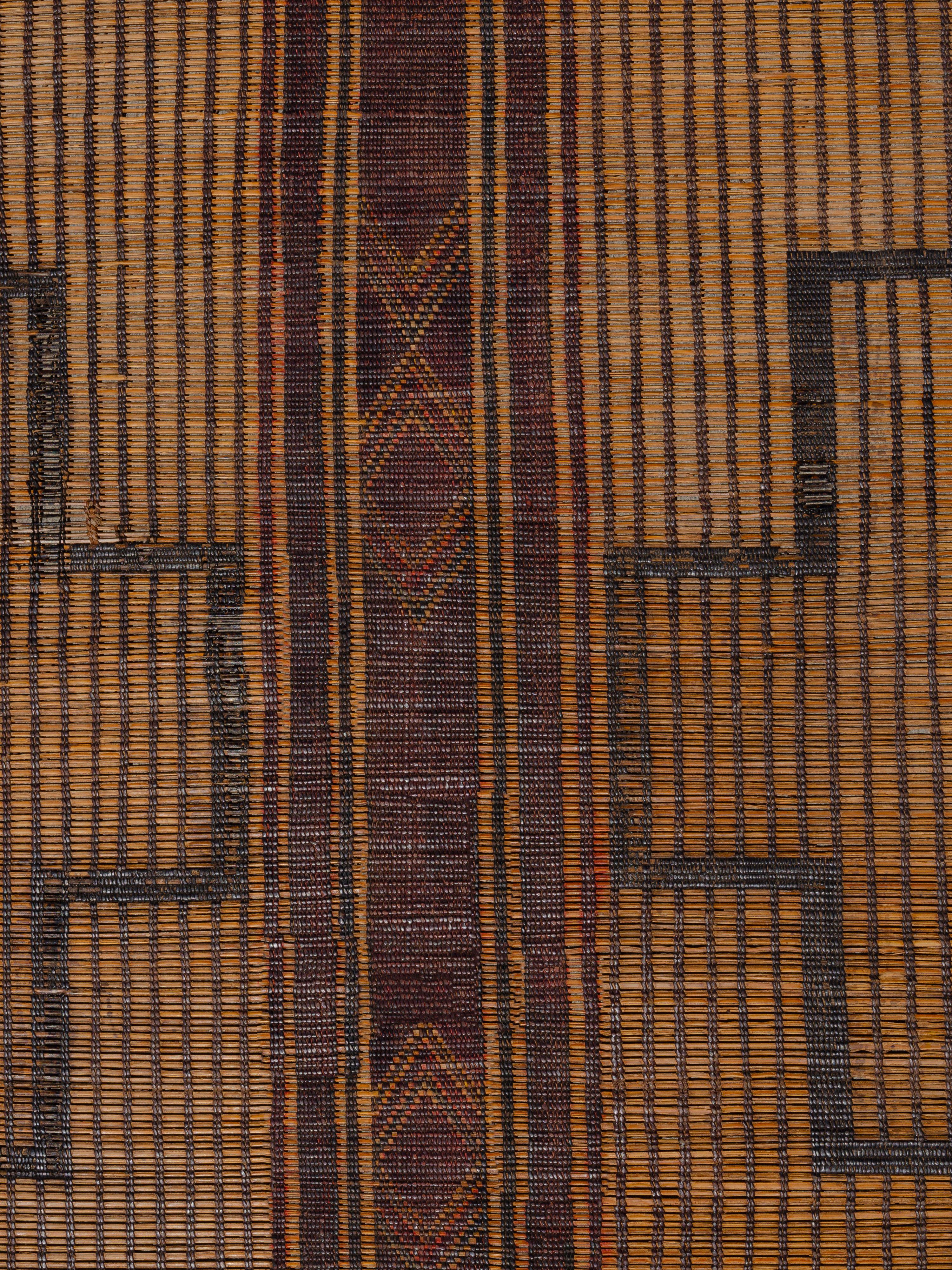 Tissés par les tribus nomades touaregs de Mauritanie avec du roseau de palmier et du cuir, ces tapis offrent une alternative texturale aux revêtements de sol traditionnels en textile tissé. Cette pièce présente une composition plutôt symétrique de