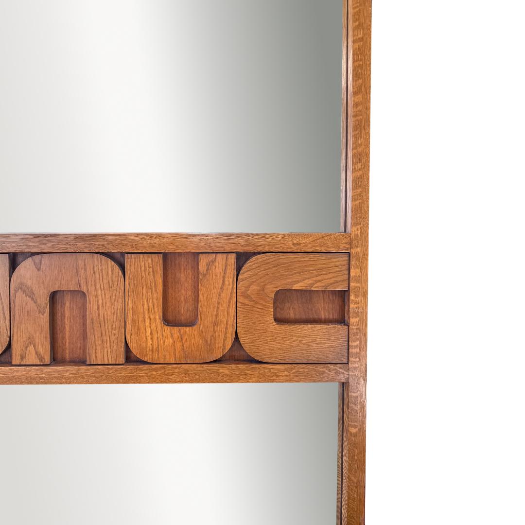 Mélange audacieux de charme du milieu du siècle et de style rétro-futuriste, ce double miroir vintage présente un cadre en bois de noyer aux lignes épurées et modernes. Une garniture sculpturale centrale distinctive divise le miroir en deux vitres,