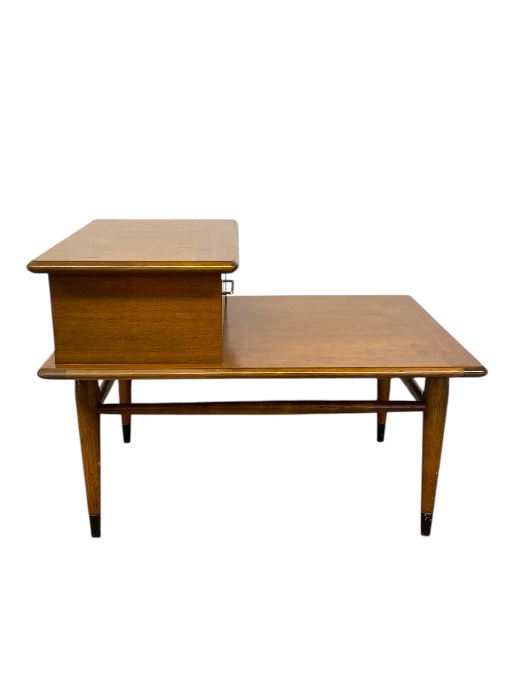 Table d'appoint vintage de Lane Furniture, datant du milieu du 20e siècle et emblématique du design moderne classique américain du milieu du siècle. Fabriquée en noyer et placage de noyer, la table présente une forme étagée à deux niveaux qui offre