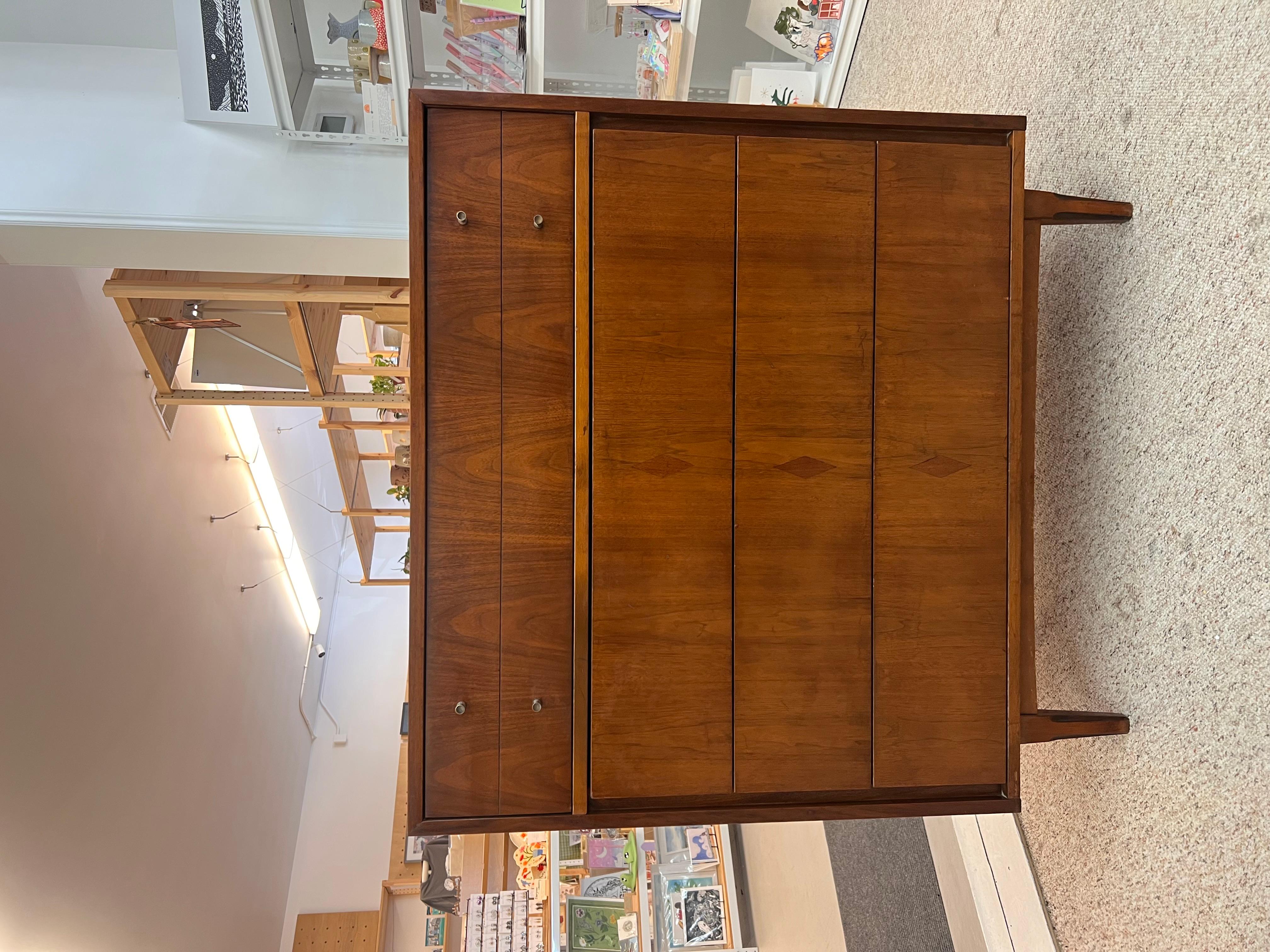 This mid-century dresser features a clean and minimalist design typical of the era. It has a warm wood finish, likely made from walnut or another hardwood, showcasing the natural grain. The dresser is structured with four drawers. The top drawers is