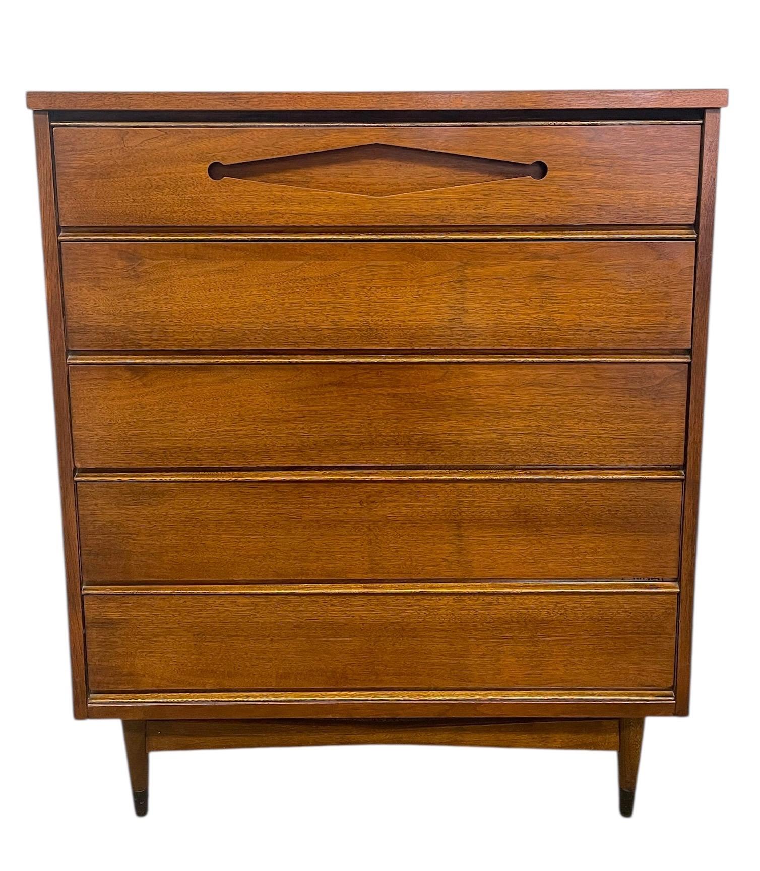 Un comò vintage del Mid Century Modern dalle linee pulite di ispirazione danese e dal design funzionale. Questo mobile offre cinque cassetti spaziosi, il cui piano è impreziosito da un caratteristico tiretto scolpito a forma di diamante affiancato