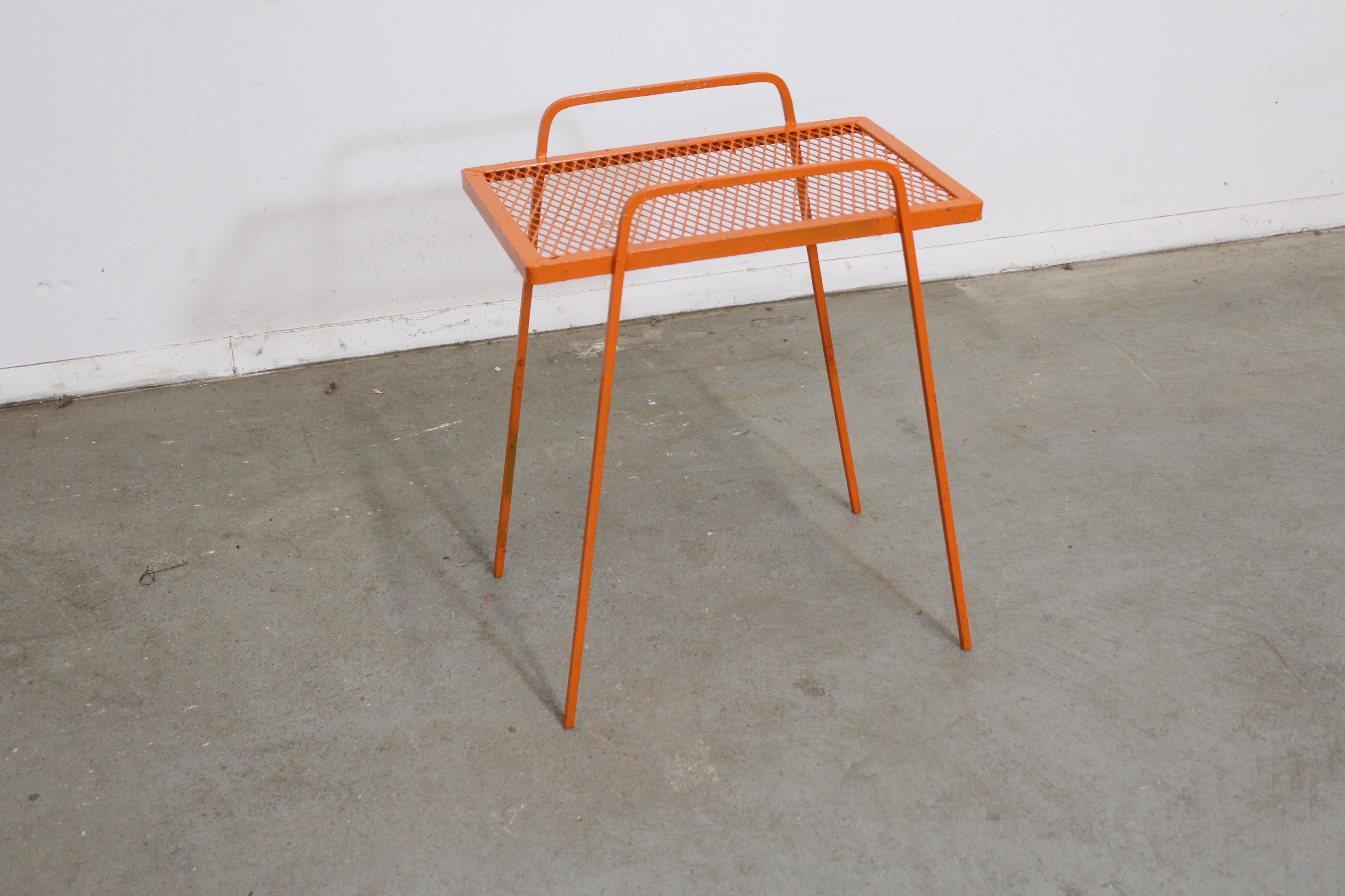 Offered is a vintage Mid-Century Modern atomic orange metal tall end table, circa 1960's. This piece is made of welded steel and features gracefully styled legs and a mesh top. It is in good condition considering its age with minor age wear (surface