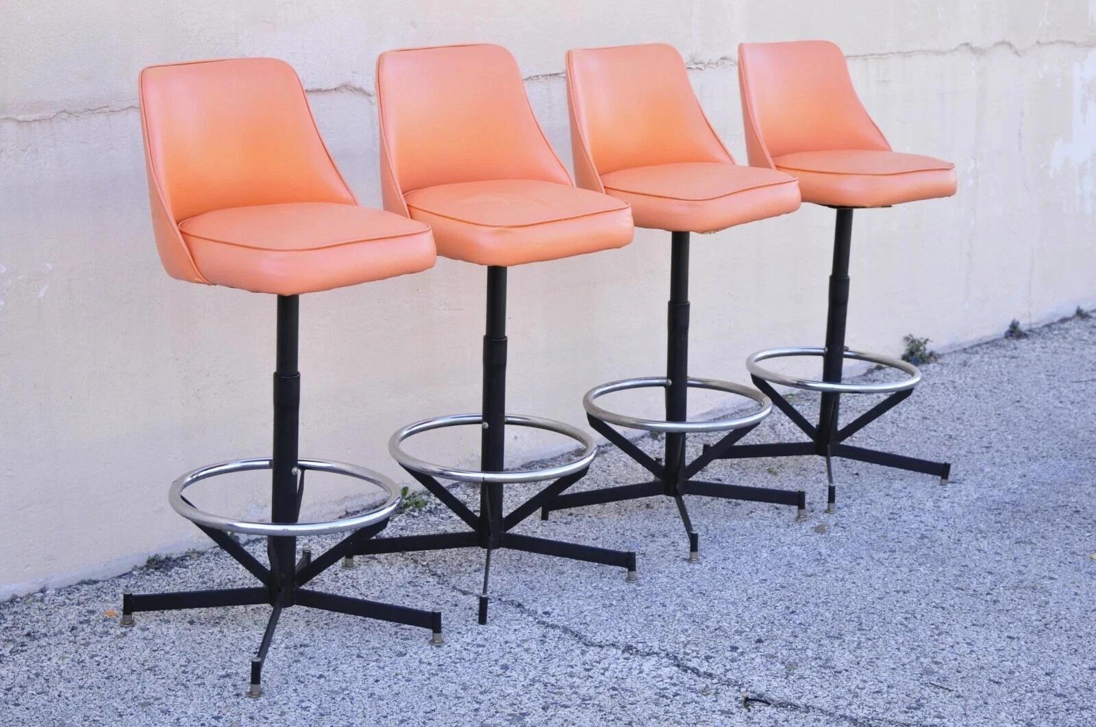 Vintage Mid Century Modern Atomic Era Vinyl Metal Adjustable Swivel Barstools - Set of 4.  L'articolo presenta sedili girevoli imbottiti in vinile arancione, 3 altezze regolabili, etichetta originale, un bel set vintage. Circa metà del XX secolo.