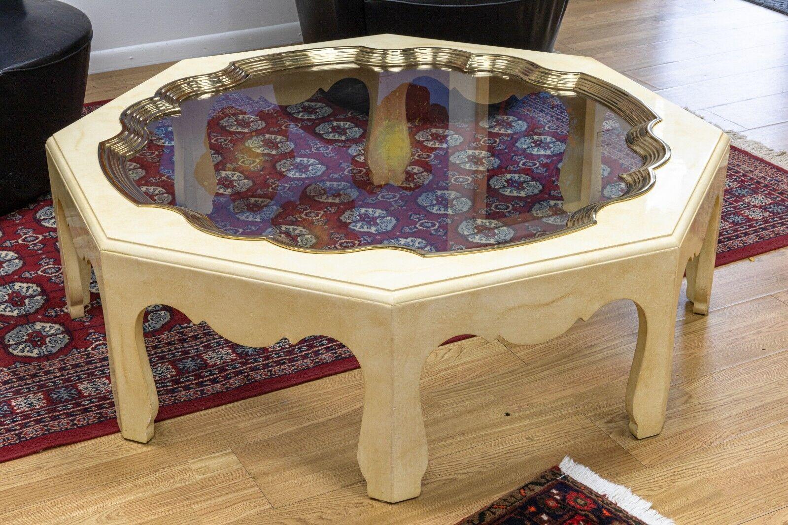 A vintage Baker Furniture octagonal coffee table. This lovely coffee table feature a drop in glass top with a ribbed brass accent, and cream painted wood base with an octagonal shape. This table is in very good condition. It measures 15.5 in tall