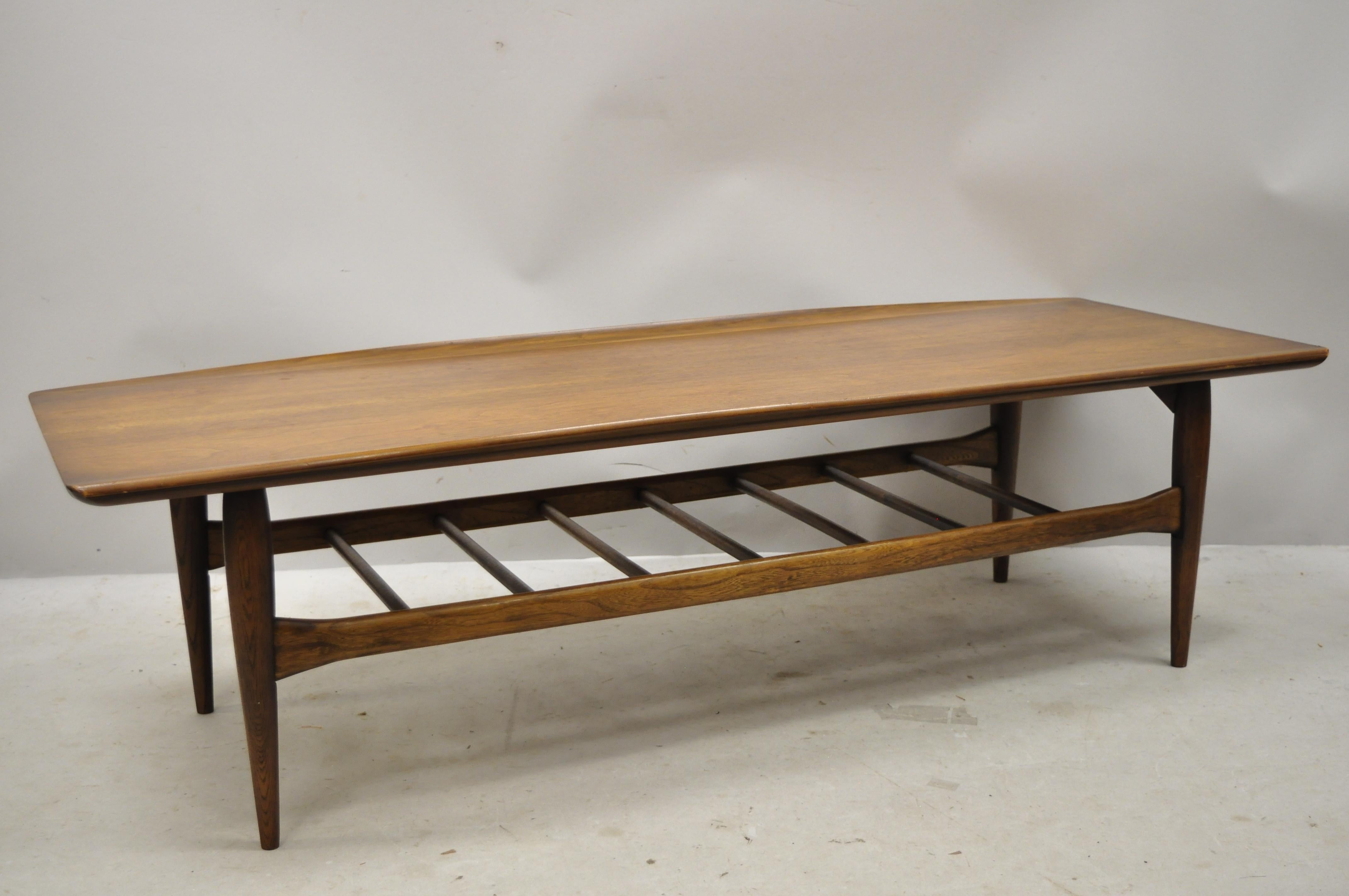 Vintage Mid-Century Modern Bassett walnut sculpted edge surfboard coffee table. Item features a spindle base lower shelf, solid wood construction, beautiful wood grain, tapered legs, very nice vintage sleek sculptural form, circa mid-20th century.