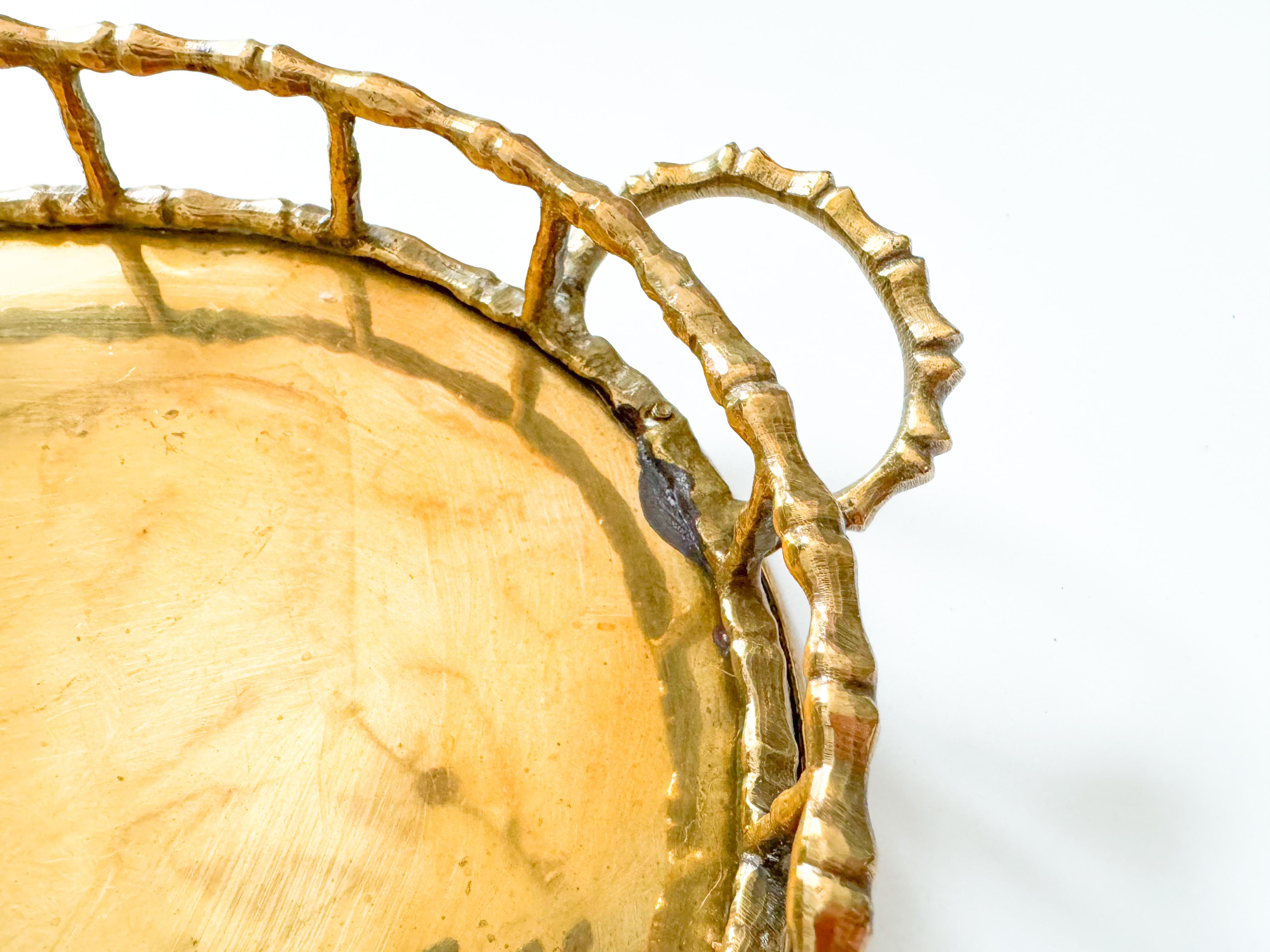 This vintage mid-century modern brass tray brings both utility and style to any space. Crafted in India during the 1950s, it features a cast brass frame designed in a faux bamboo motif—an iconic detail often associated with the Hollywood Regency