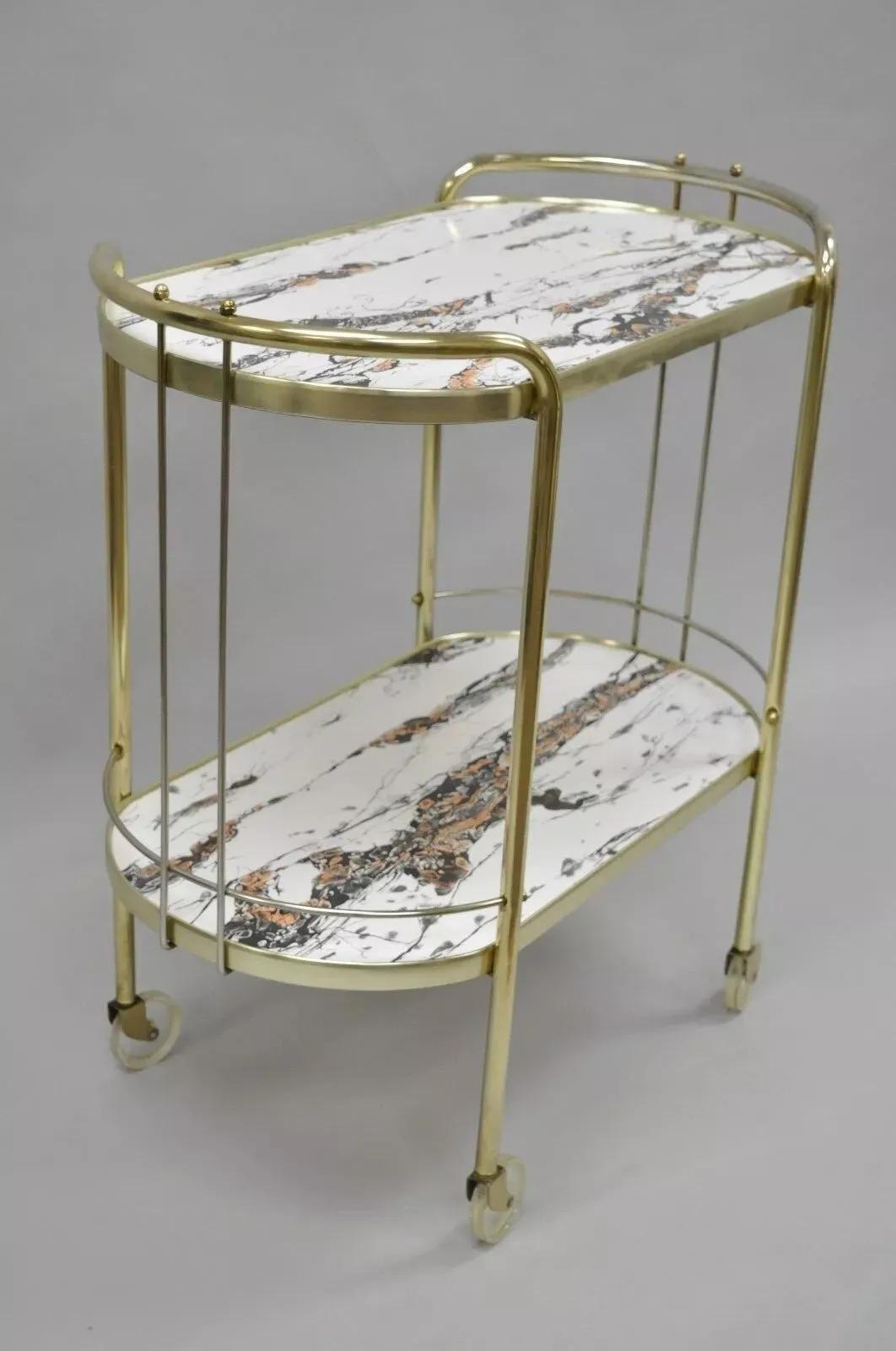 Vintage Mid Century Modern Latón Rolling Bar Tea Cart Laminado Faux Marble. El artículo cuenta con una estructura de latón de 2 niveles, ruedas giratorias, superficies laminadas de imitación de mármol y elegantes líneas modernistas. Mediados del