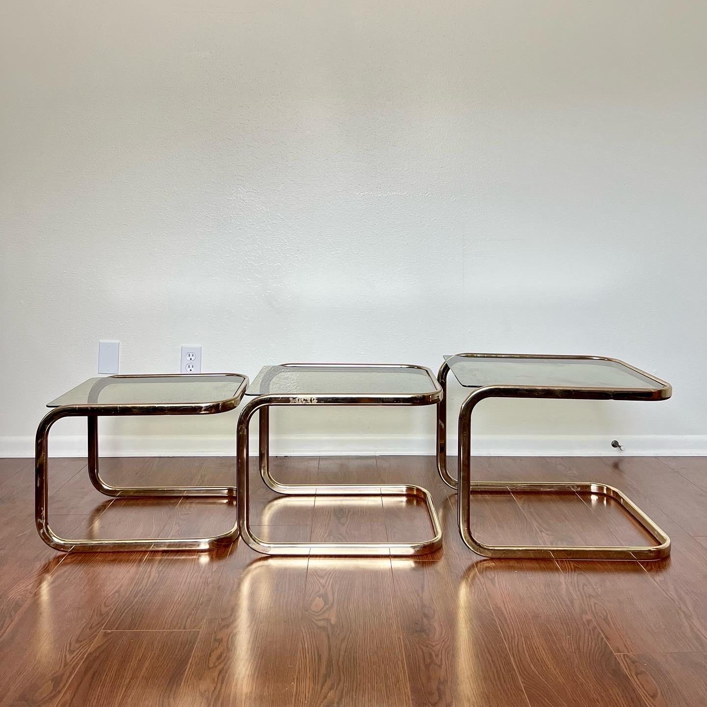 Striking Mid-Century Modern set of three brass and smoked glass nesting tables attributed to Milo Baughman for DIA. Constructed from brass plated steel with smooth, sleek frames and each featuring a plate of dark tinted glass. In good condition. No