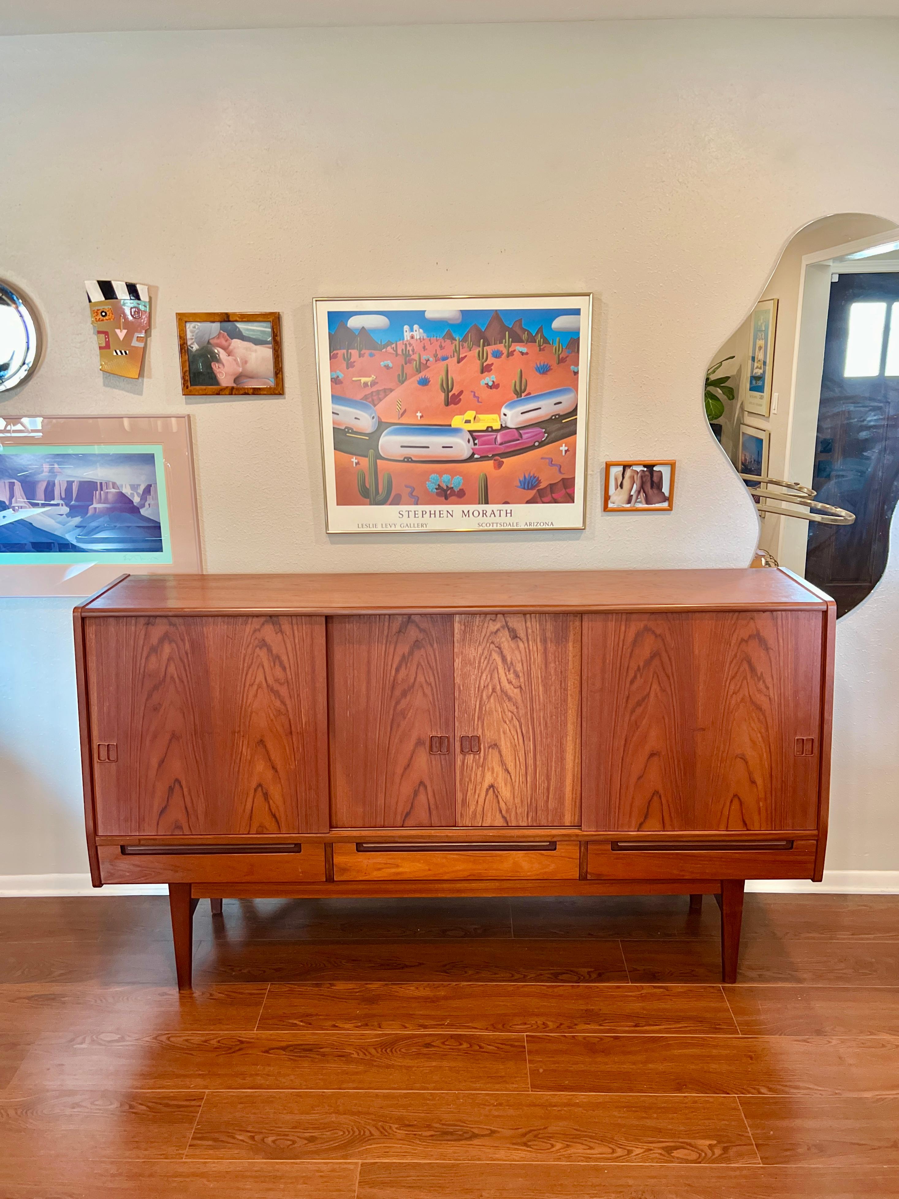 Beautiful Mid-Century Modern danish highboard. Covered with a rich teak veneer, and solid wood legs. Also has 2 sliding doors and 5 drawers, with a very MCM mirrored bar inside. Overall in very good original condition. Some minor flaws on the frame