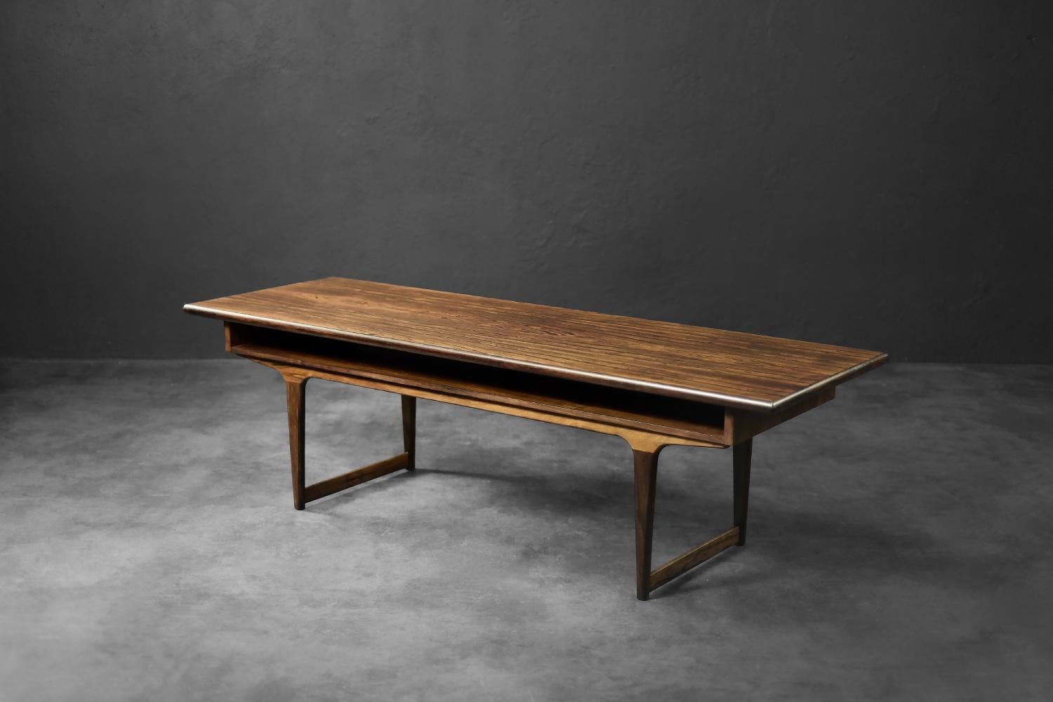 This elegant coffee table with a shelf was manufactured in Denmark during the 1960s. Crafted from high-quality, refined rosewood in a dark brown shade. The wood grain is exceptionally dynamic, distinct, and consistent. The table features an open