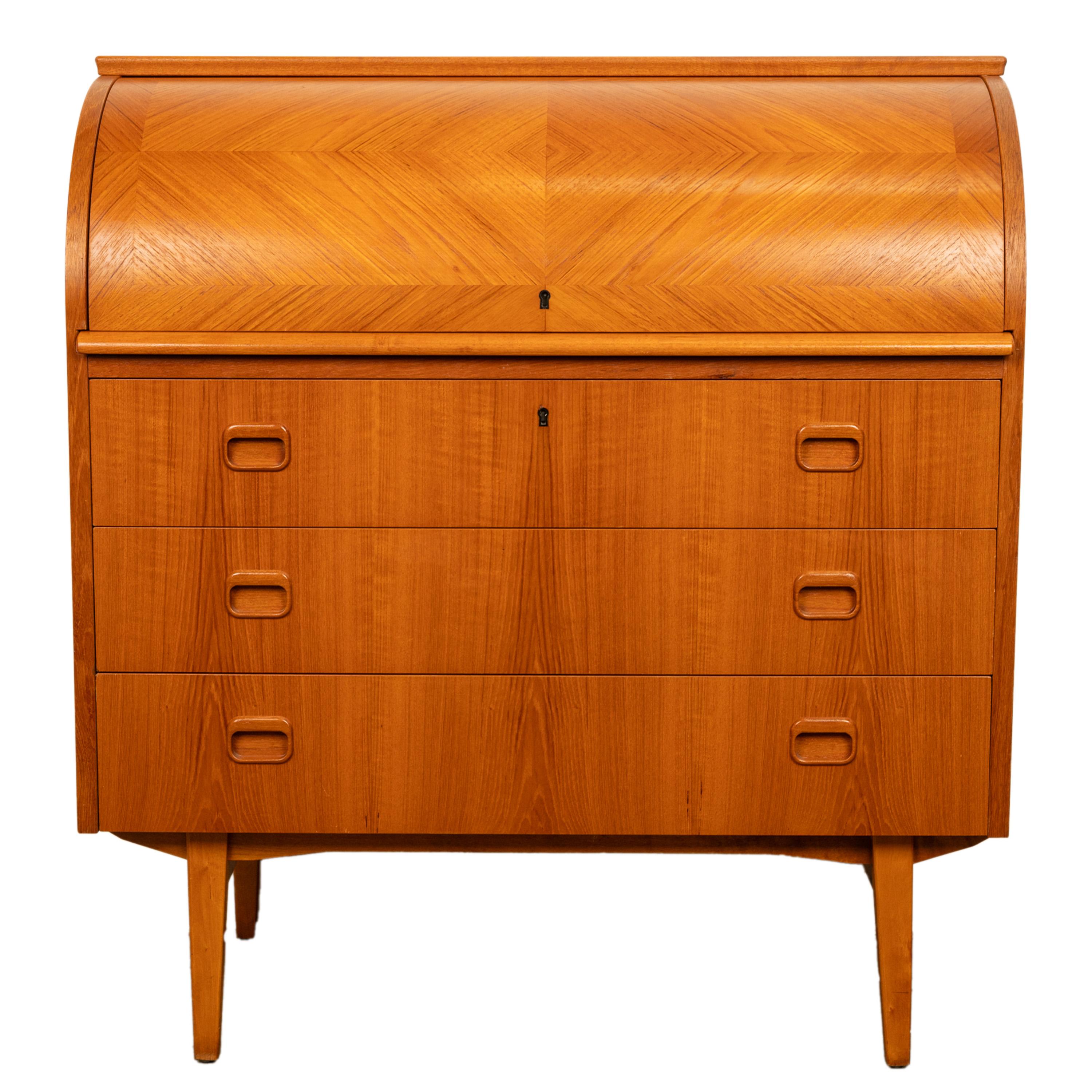 A good Mid Century Modern roll top cylinder desk bureau, circa 1968.
The desk with a locking roll top cylinder, that is cross-banded with teak, the interior is fitted with a single drawer and seven file/pigeon holes. Below are three drawers with