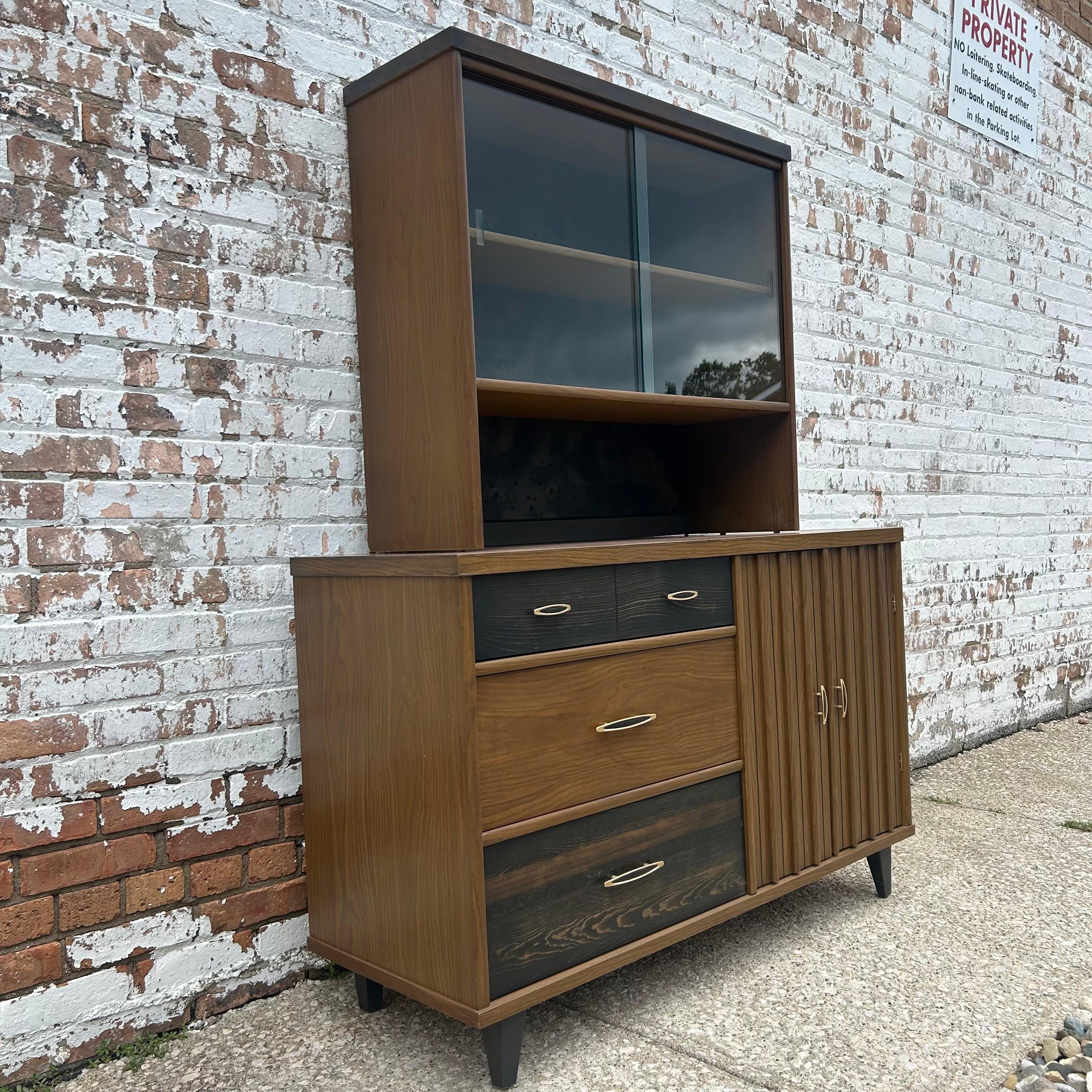 Mid-Century Modern with a twist, we love the distinctive style of this vintage cabinet. The two-piece hutch features plenty of storage and display space. She is composed of solid wood with a decorative laminate veneer in excellent quality. We love