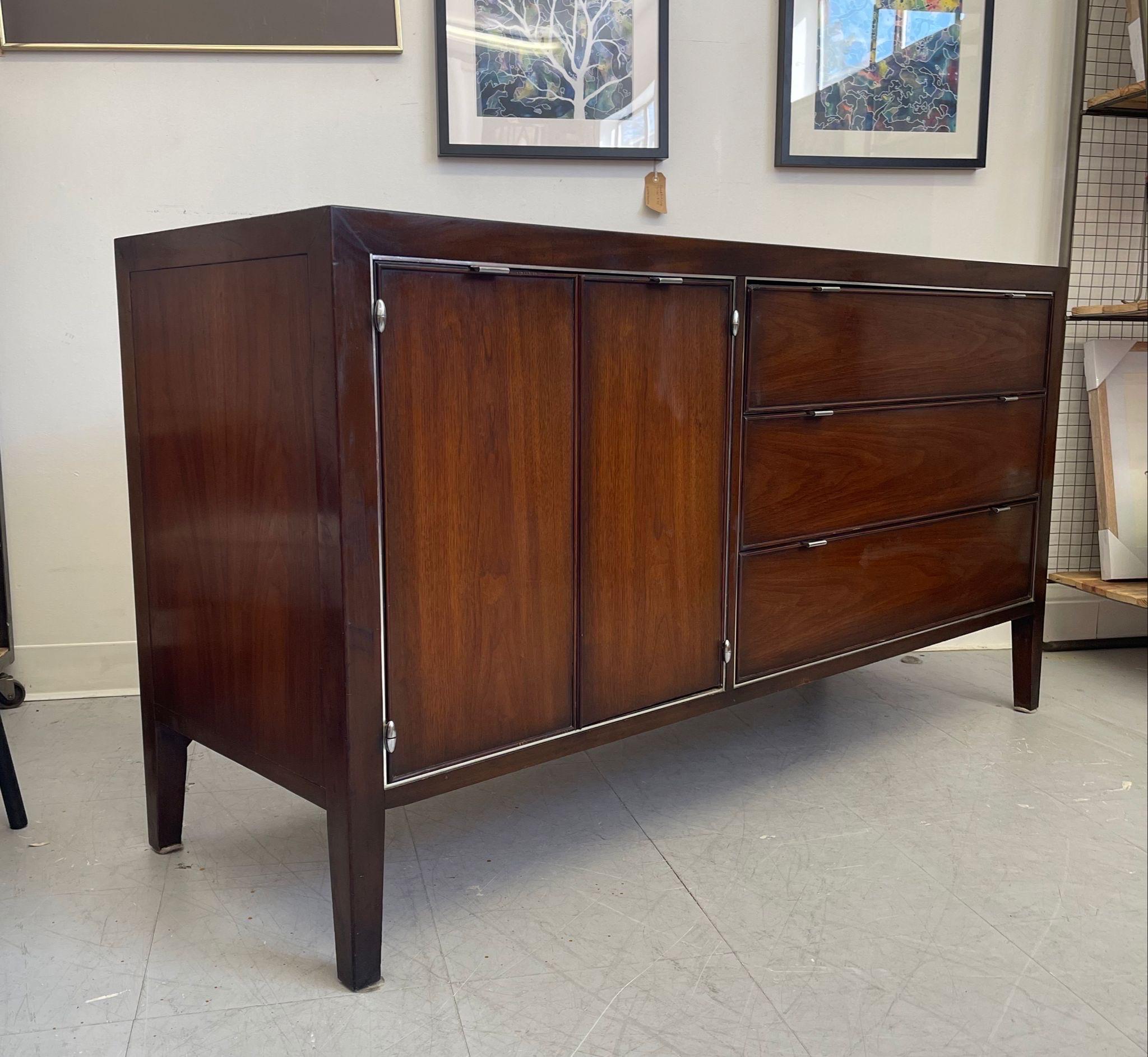 Walnut Toned Credenza with 6 dovetailed drawers. 3 Drawers are behind hinge doors.Makers mark inside drawer. Chrome toned handles. Vintage Condition Consistent with Age as Pictured.

Dimensions. 56 W ; 19 D ; 30 H
