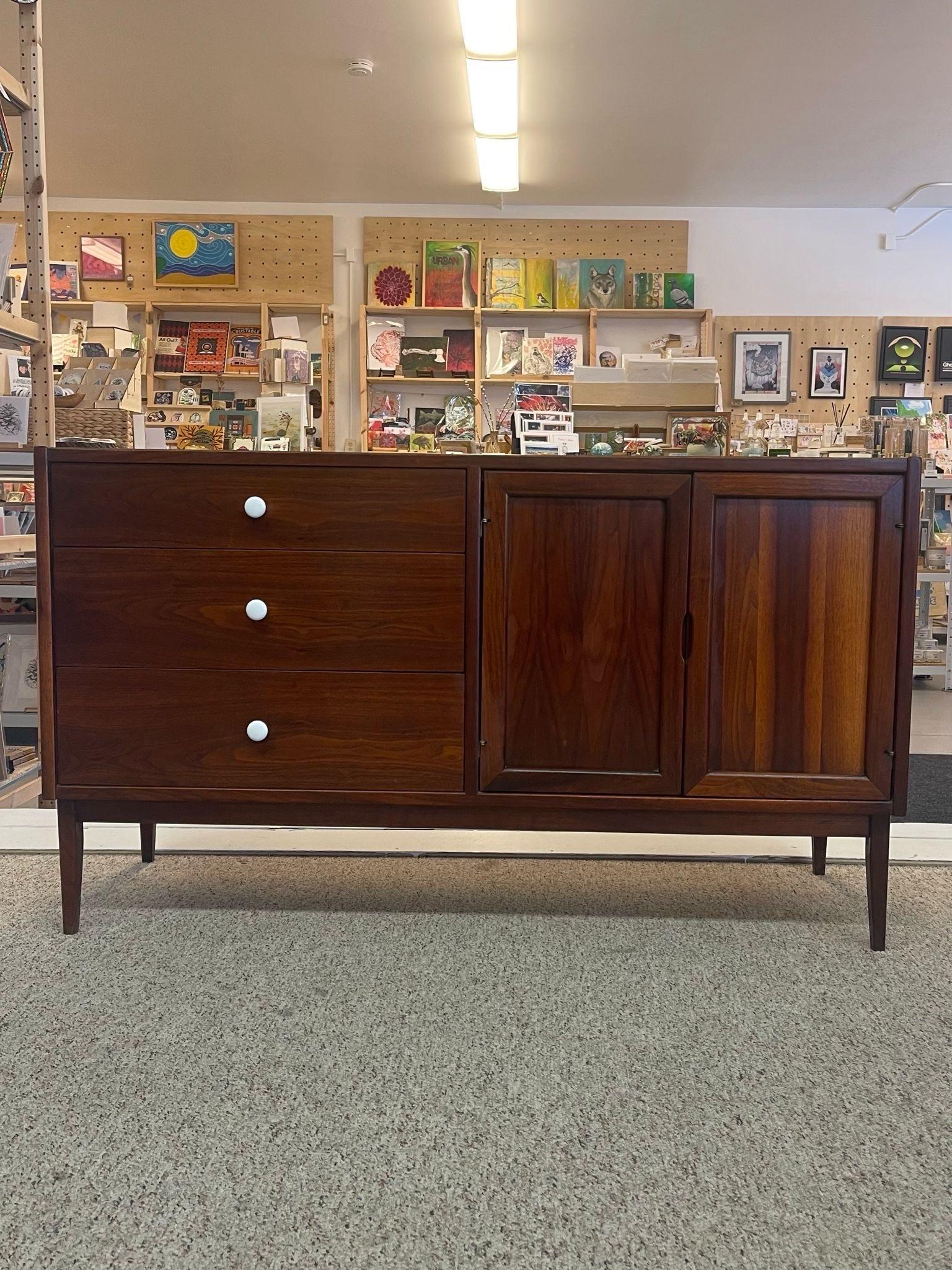 This Dresser features 3 dovetailed drawers with original white toned hardware next to two hinge doors opening to cabinet space with one adjustable shelf. Tapered legs.
We believed this to be a Drexel piece due to construction, design and overall