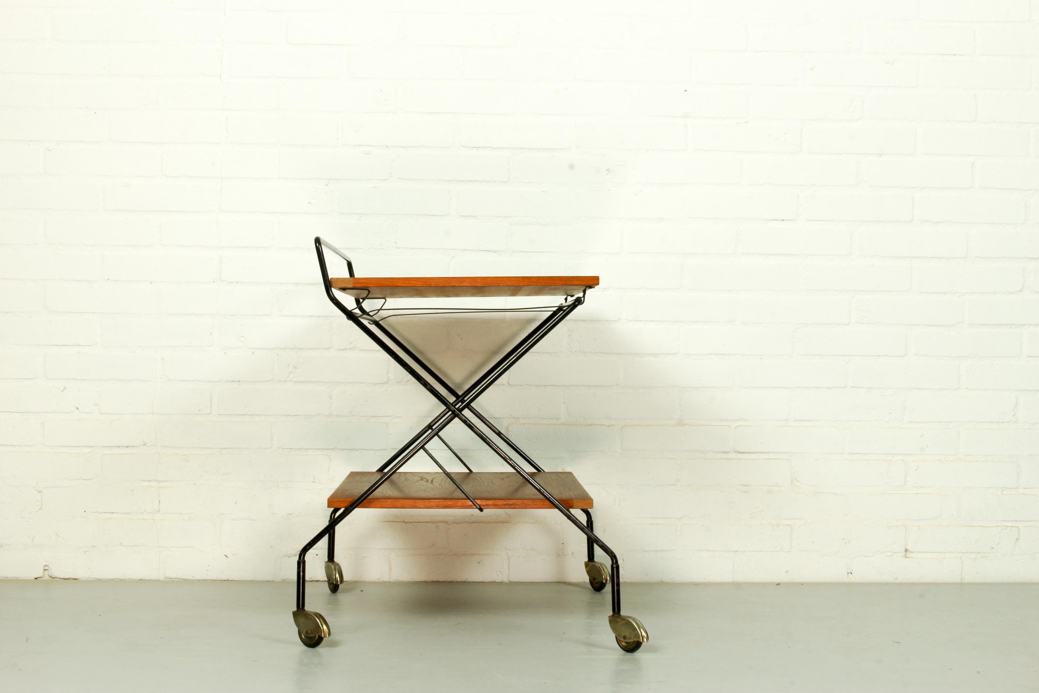 Vintage tea trolley from the 1960s. The cart has 2 teak blades, a black metal frame and stands on metal wheels. A special feature of this model is that it is foldable.
 