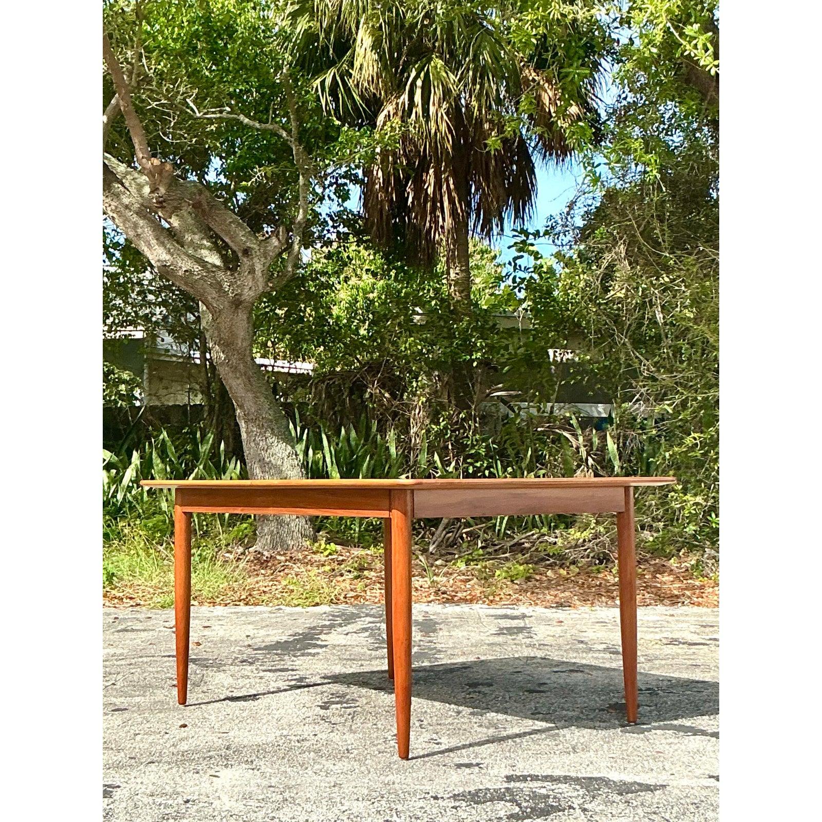 Dieser exquisite, ausziehbare Esstisch aus der Mitte des Jahrhunderts besticht durch schlanke Handwerkskunst und zeitlose Eleganz. Die warme Holzmaserung unterstreicht die raffinierte Ausstrahlung, während die minimalistischen, konisch zulaufenden