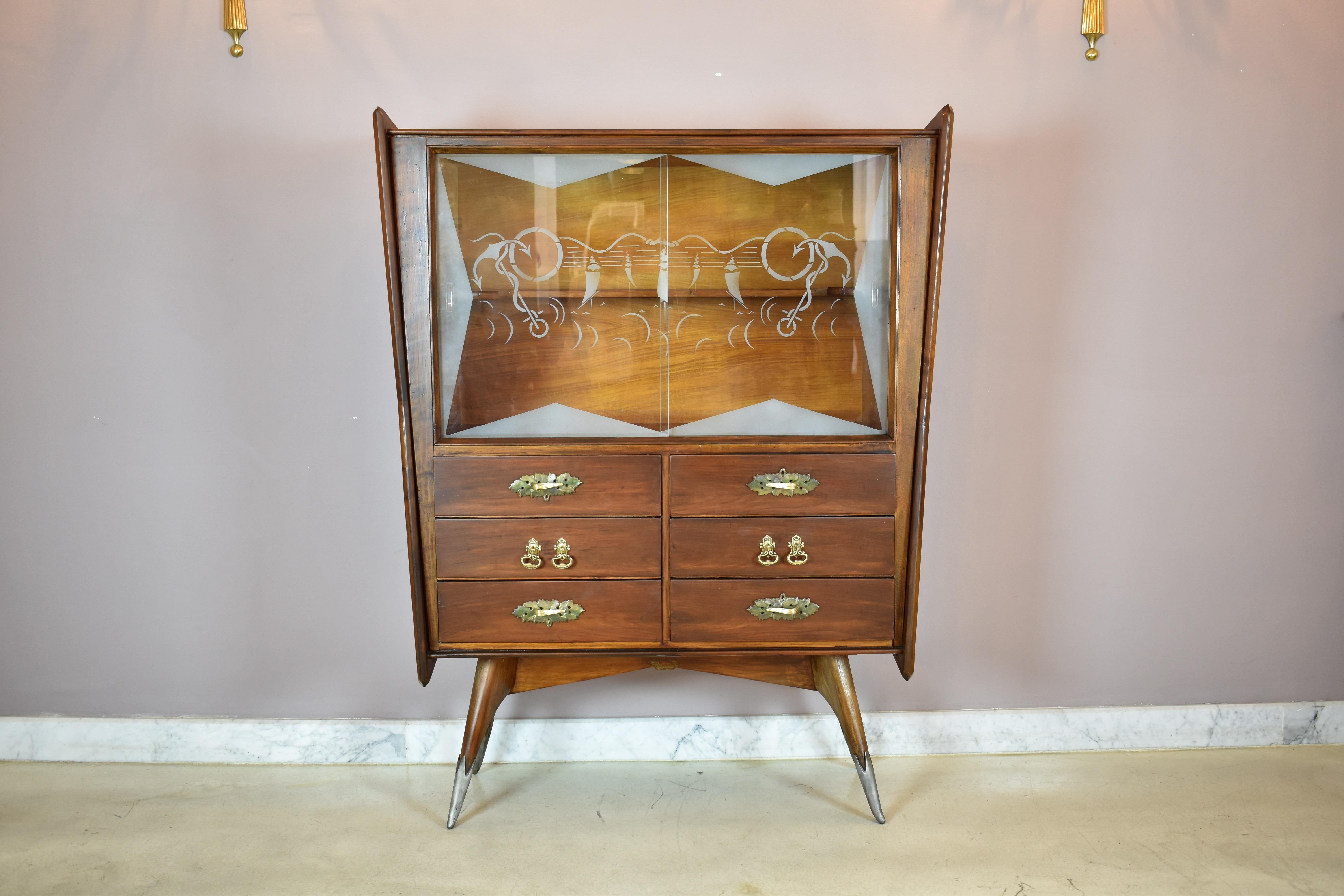 A stunning Italian mid-century modern vintage cabinet with an angular design and exquisite craftsmanship. 
This 1950s piece features intricate etched glass slideable doors with graceful swirling nautical patterns. The cabinet's rich wood veneer is