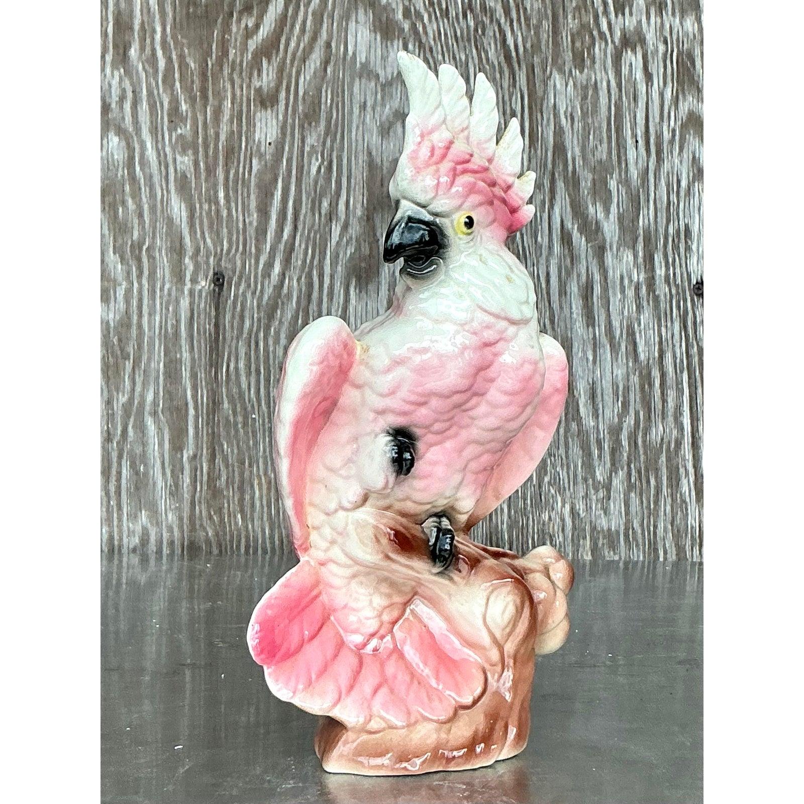 Ajoutez une touche de charme tropical à votre décor avec cette figurine de cacatoès en céramique vintage du milieu du siècle. Elegamment perché sur une branche d'arbre, cet oiseau émaillé à la main arbore une palette rose et blanche éclatante, avec