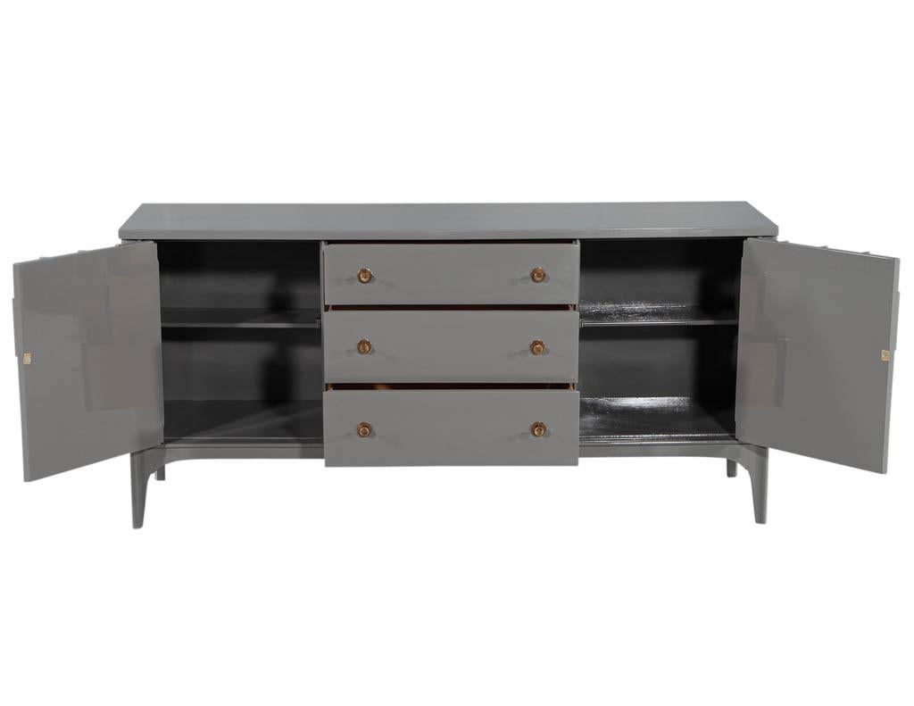 Vintage Mid-Century Modern grey lacquered buffet sideboard. Masterfully restored by the artisans at Carrocel in a modern grey lacquered finish. Complete with unique architectural detailing with round brass handles. Ample storage options with 3 large