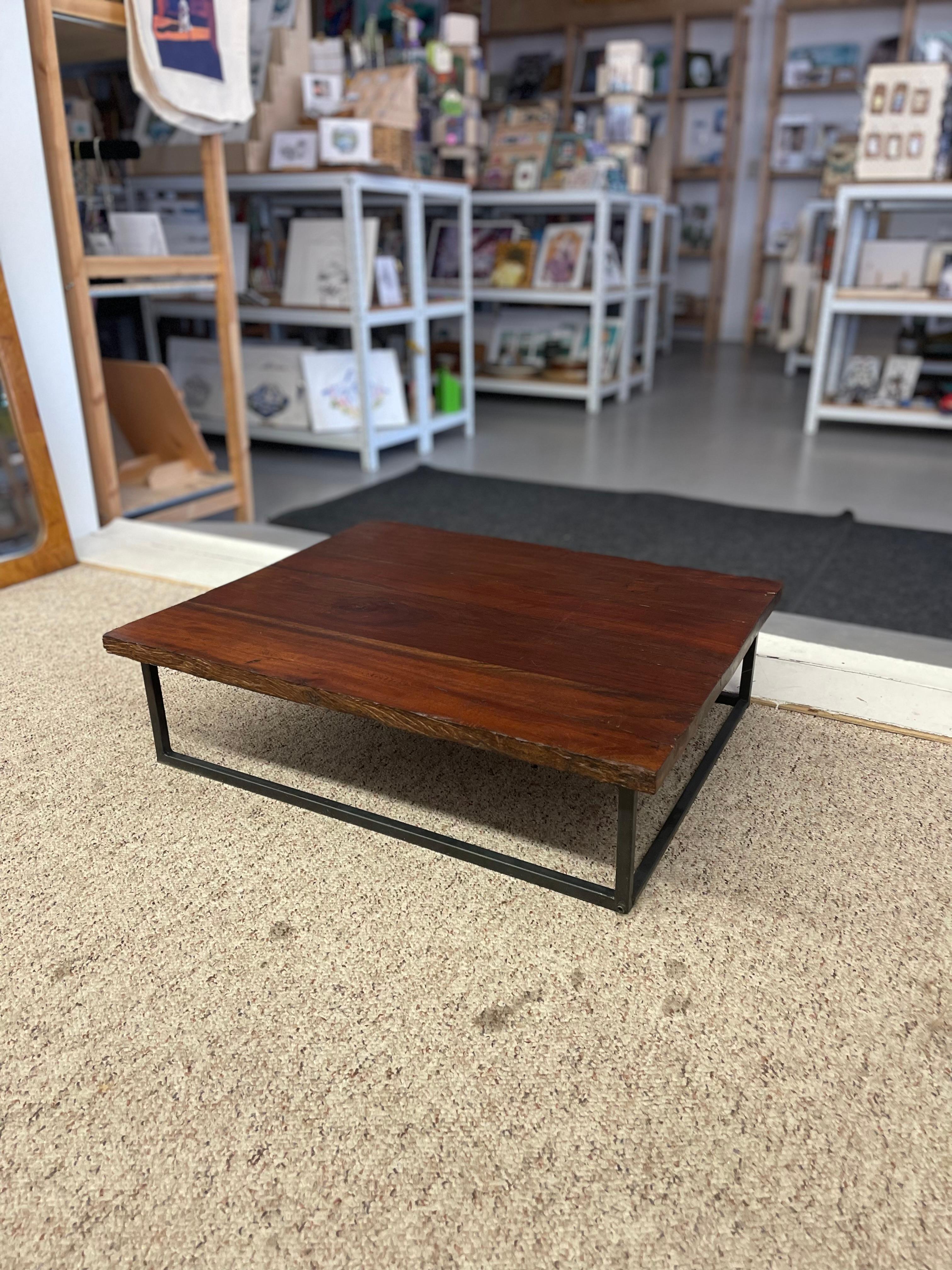  This low-profile coffee table features a thick, solid wood slab top with natural grain variation, knots, and surface character consistent with reclaimed or minimally processed wood. The rich reddish-brown finish highlights the wood's natural