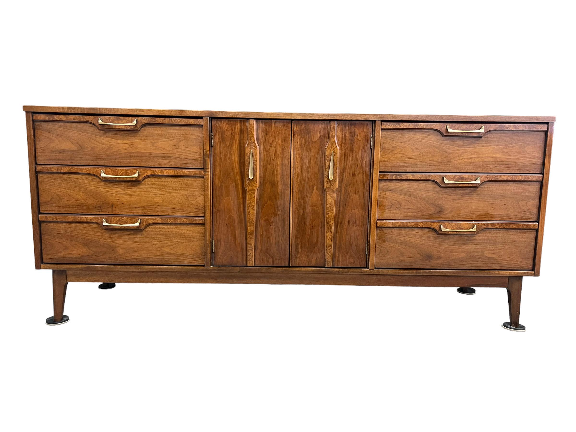 This MCM Nine Drawer Walnut Dresser Features Contrasting Wood Veneer Accents , Solid Brass Hardware and Gorgeous Wood Grain. This Six Feet Long Dresser Rests on Tapered Legs Connected to an Apron and is Structurally Sound with Smooth Sliding