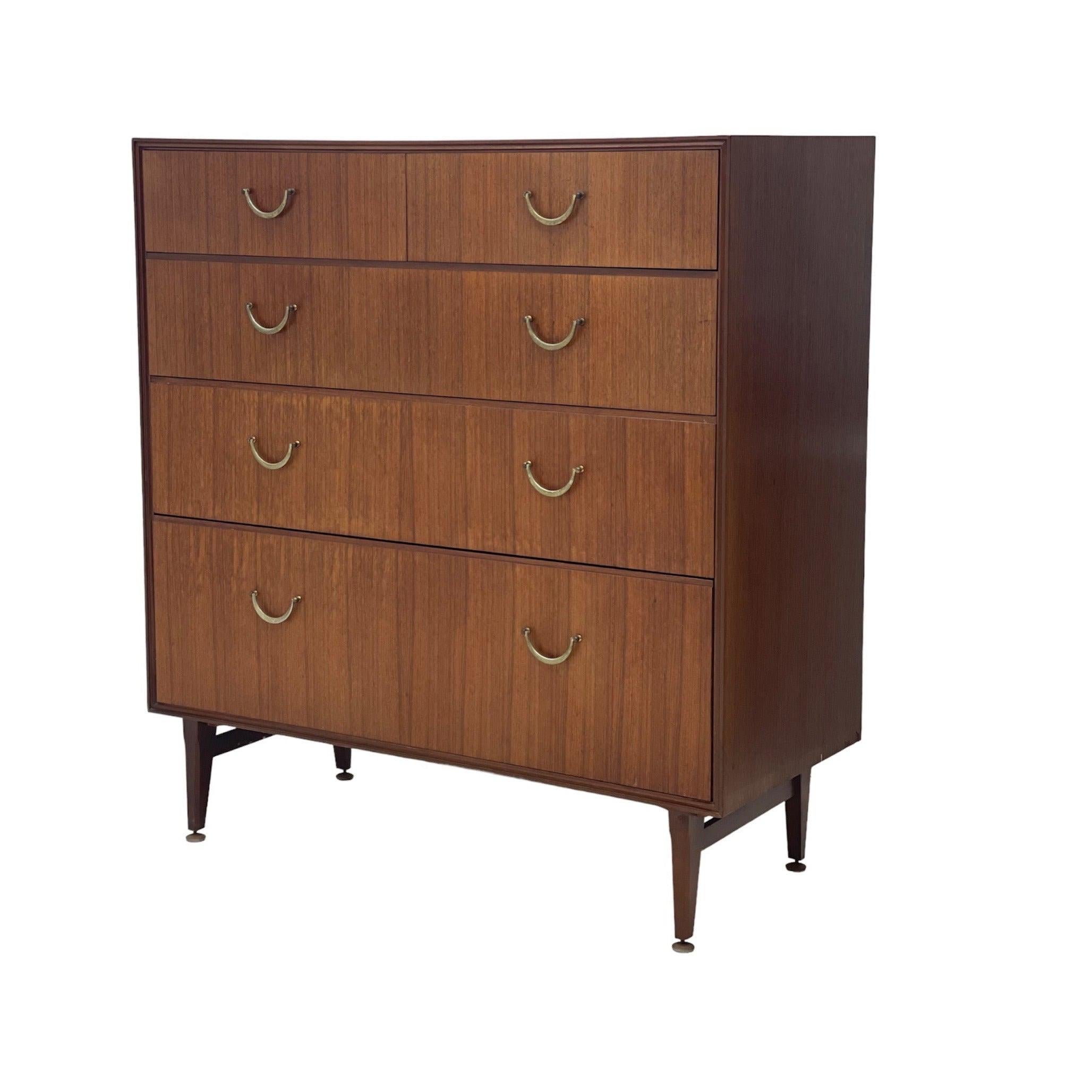 Importation récente au Royaume-Uni de cette commode à 5 tiroirs, probablement datant des années 1970, dans le style de la marque britannique Mere-dew, avec un grain de bois vertical élégant, des poignées en laiton en forme de U et de grands pieds