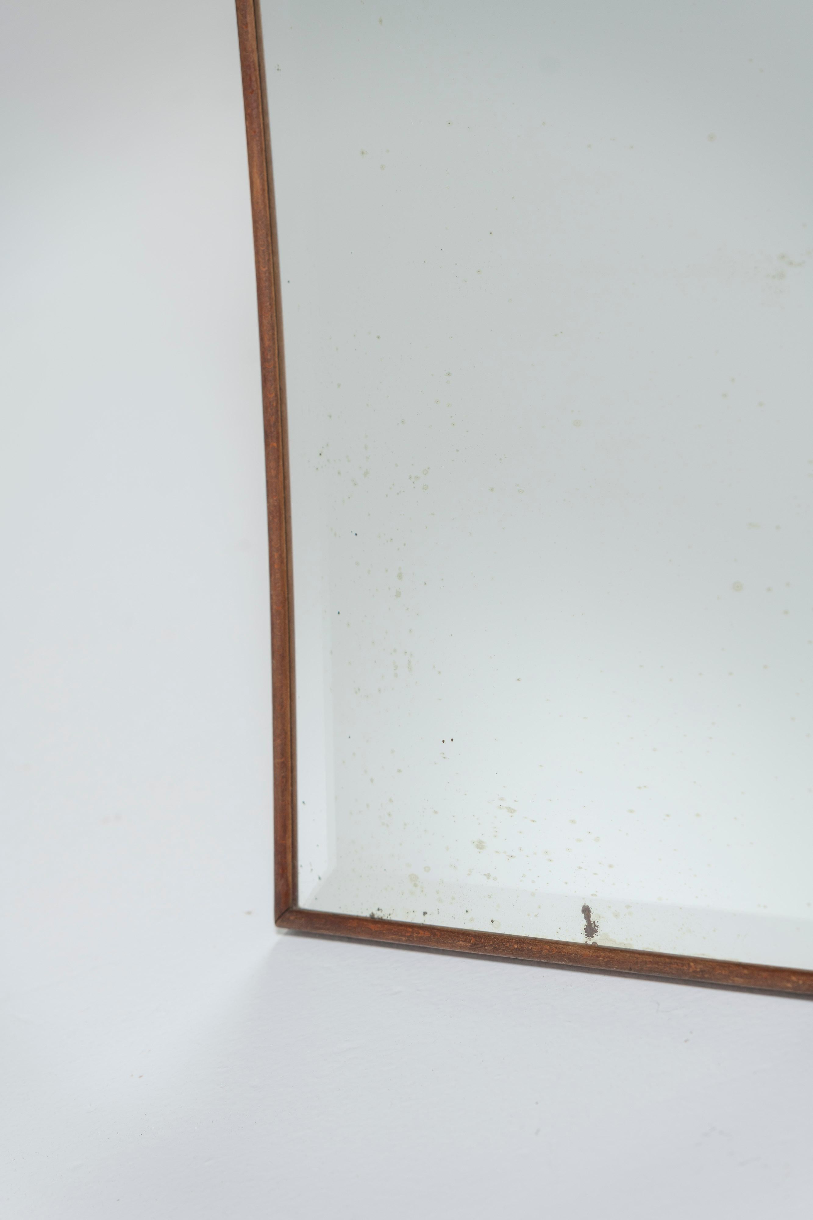 Vintage Mid-Century Modern mirror is made of beveled ground glass and beautifully framed in wood. The top and sides are gently curved, offering more than a typical rectangular shape to its perfect spot. Some minor fading in the mirror, consistent