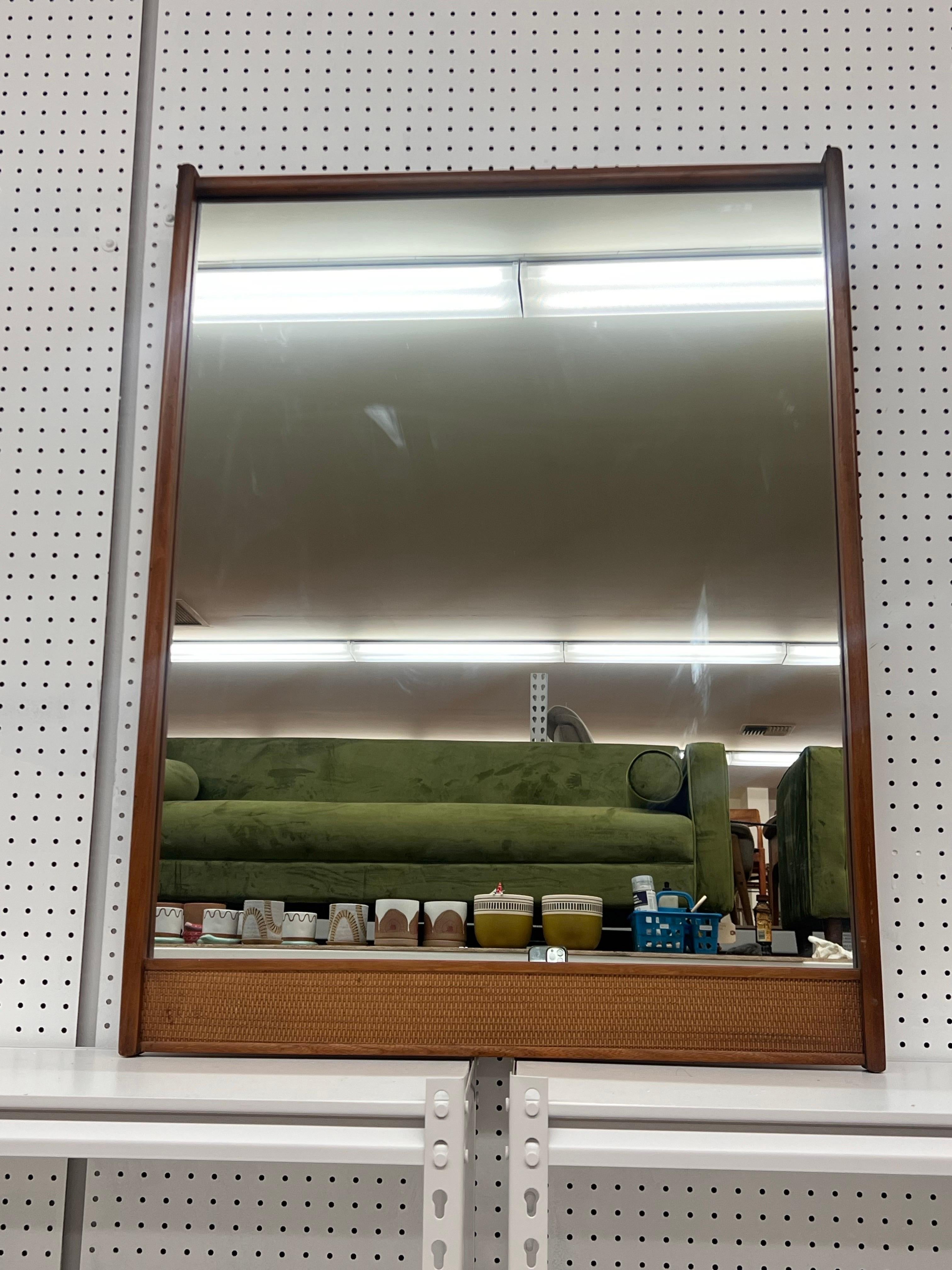 L'image présente un miroir moderne du milieu du siècle, caractérisé par ses lignes épurées et son design minimaliste. Le cadre est en bois avec une finition chaleureuse, mettant en valeur une silhouette simple mais élégante. La partie inférieure du