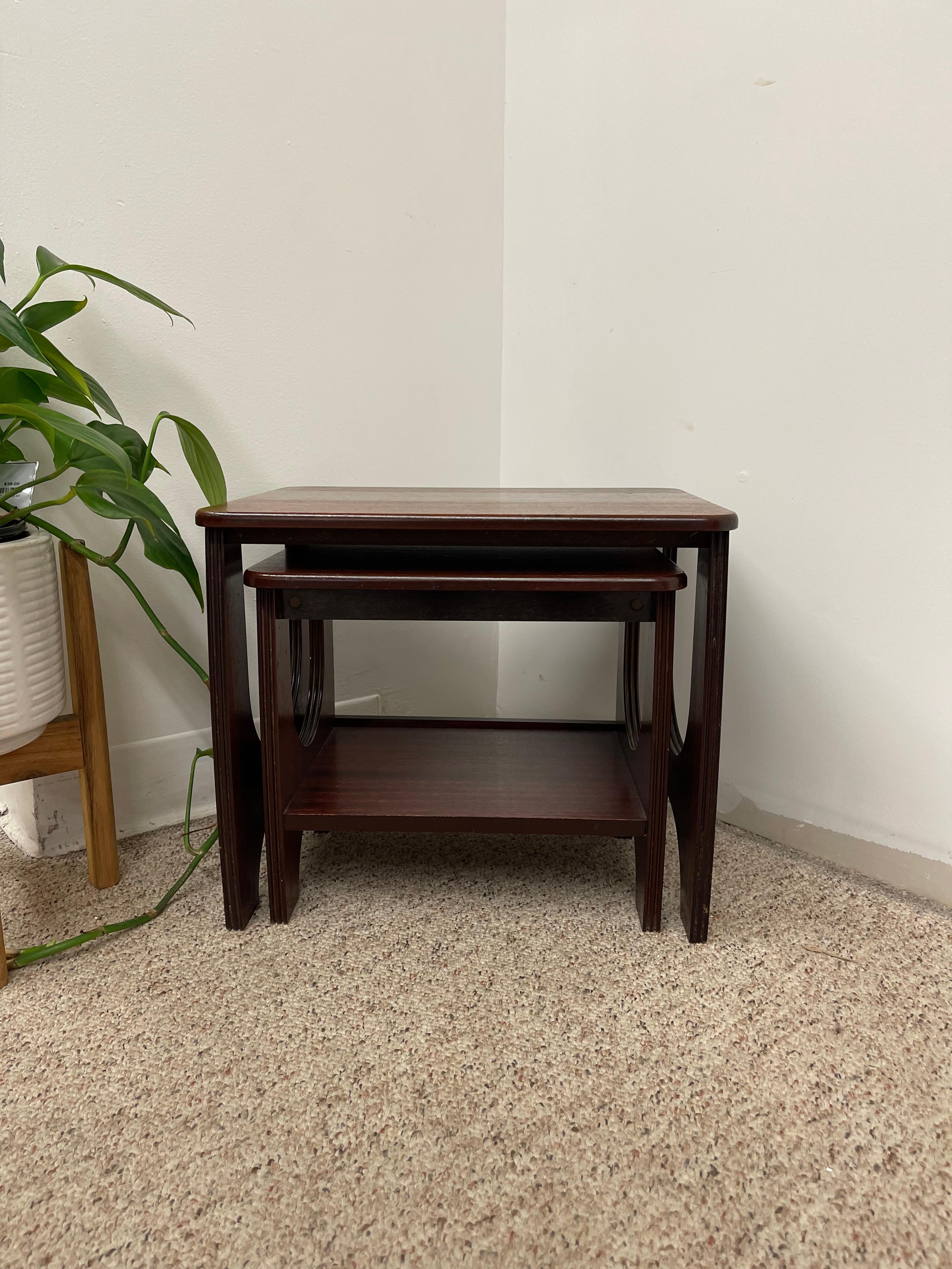  This elegant set of two vintage mid-century modern nesting tables features a rich dark finish and sculptural side profiles with arched cutouts. Designed for both function and form, the smaller table slides neatly beneath the larger one, offering