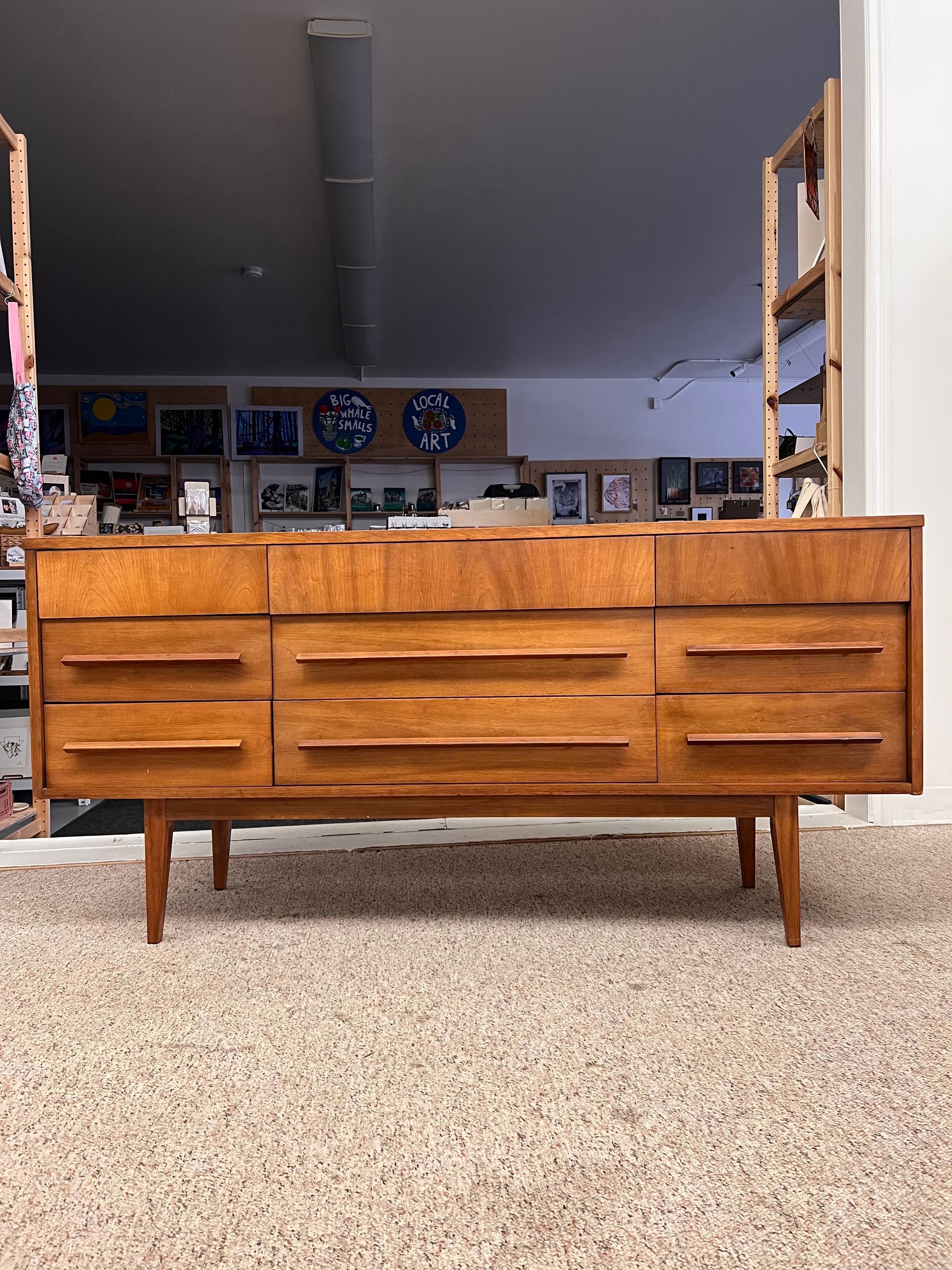 Vintage Mid-Century Modern Credenza dresser by Dixie Furniture. Dresser contains Cherry wood with nine drawers on raised legs set on apron. Great design elements top drawers protruding out with cut out handle slots under the drawer fronts having