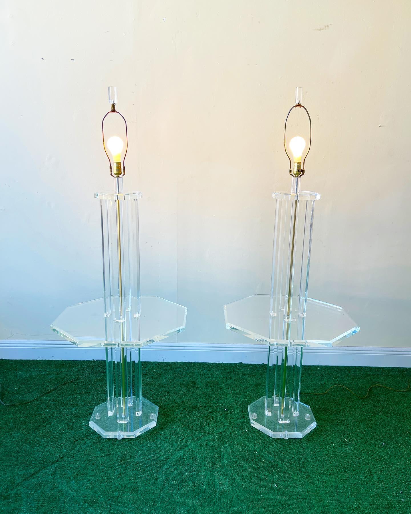 Pair of mid-century lucite floor lamps with octagonal table shelf. Classic 1970s Lucite in very good condition. The four part column center with octagonal table shelf is supported by a square base with clipped corners.
The wires run up through the