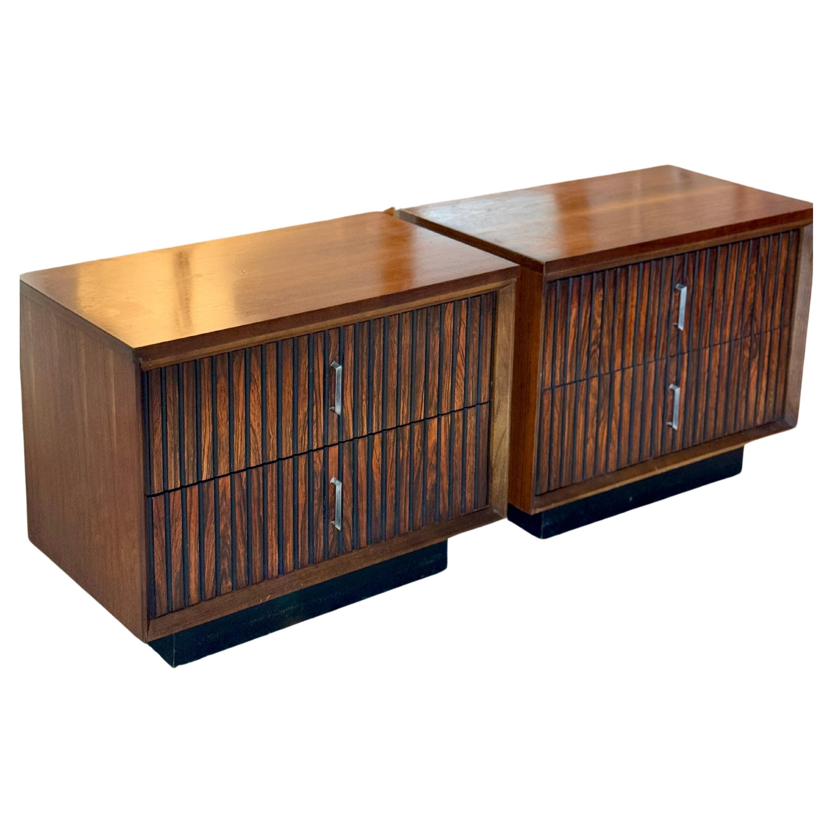 Vintage mid century modern pair of nightstands by Basset Furniture Co., circa 1960s. These have ribbed walnut and faux rosewood veneered drawers with sleek black pinstripe accents, resting on a black plinth base. Overall in good original condition