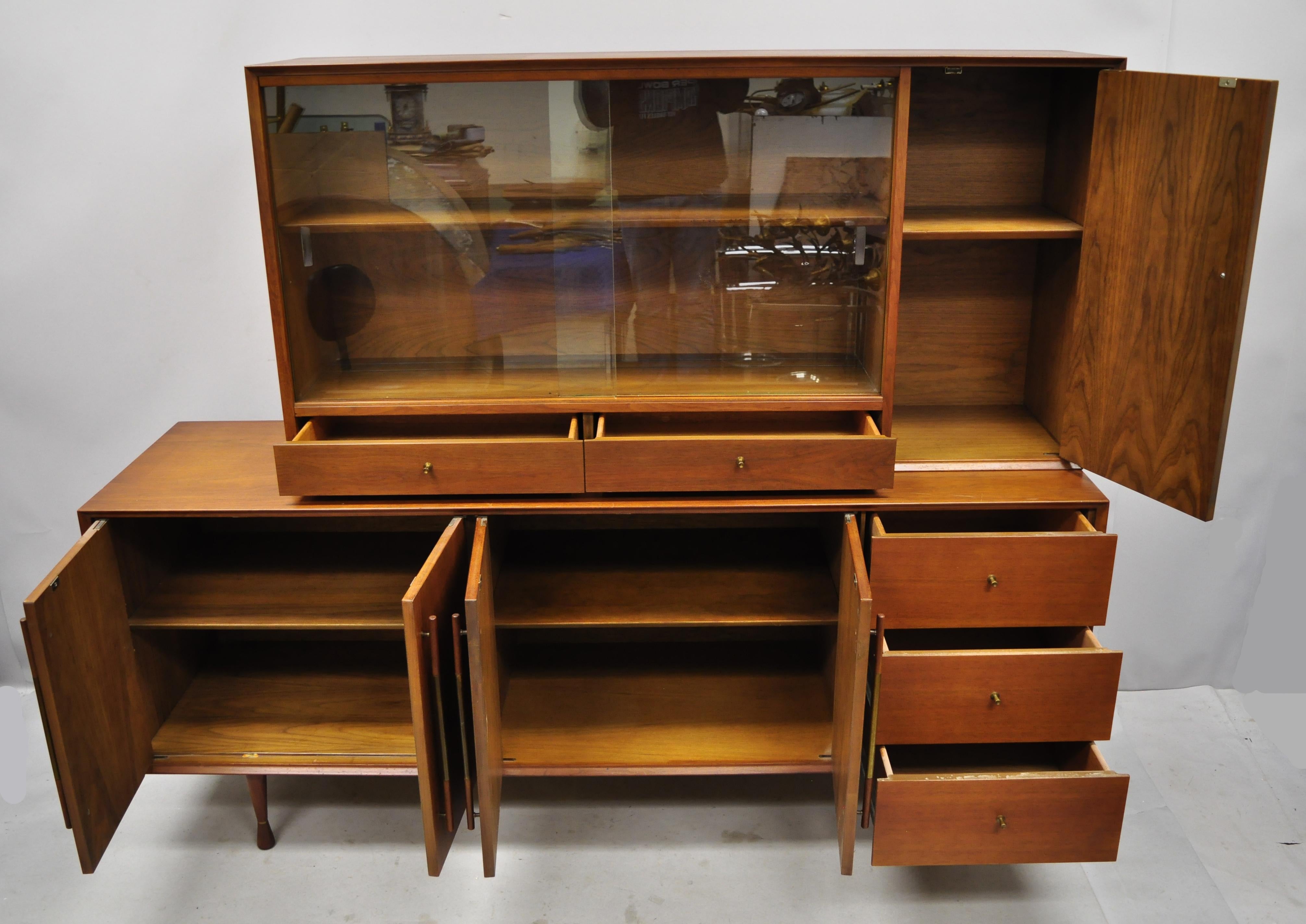 Vintage Mid-Century Modern Paul McCobb style walnut credenza hutch China cabinet. Listing includes hourglass shaped legs, brass accents and hardware, 2 sliding glass doors, beautiful wood grain, 2 part construction, 4 swing doors, 5 dovetailed