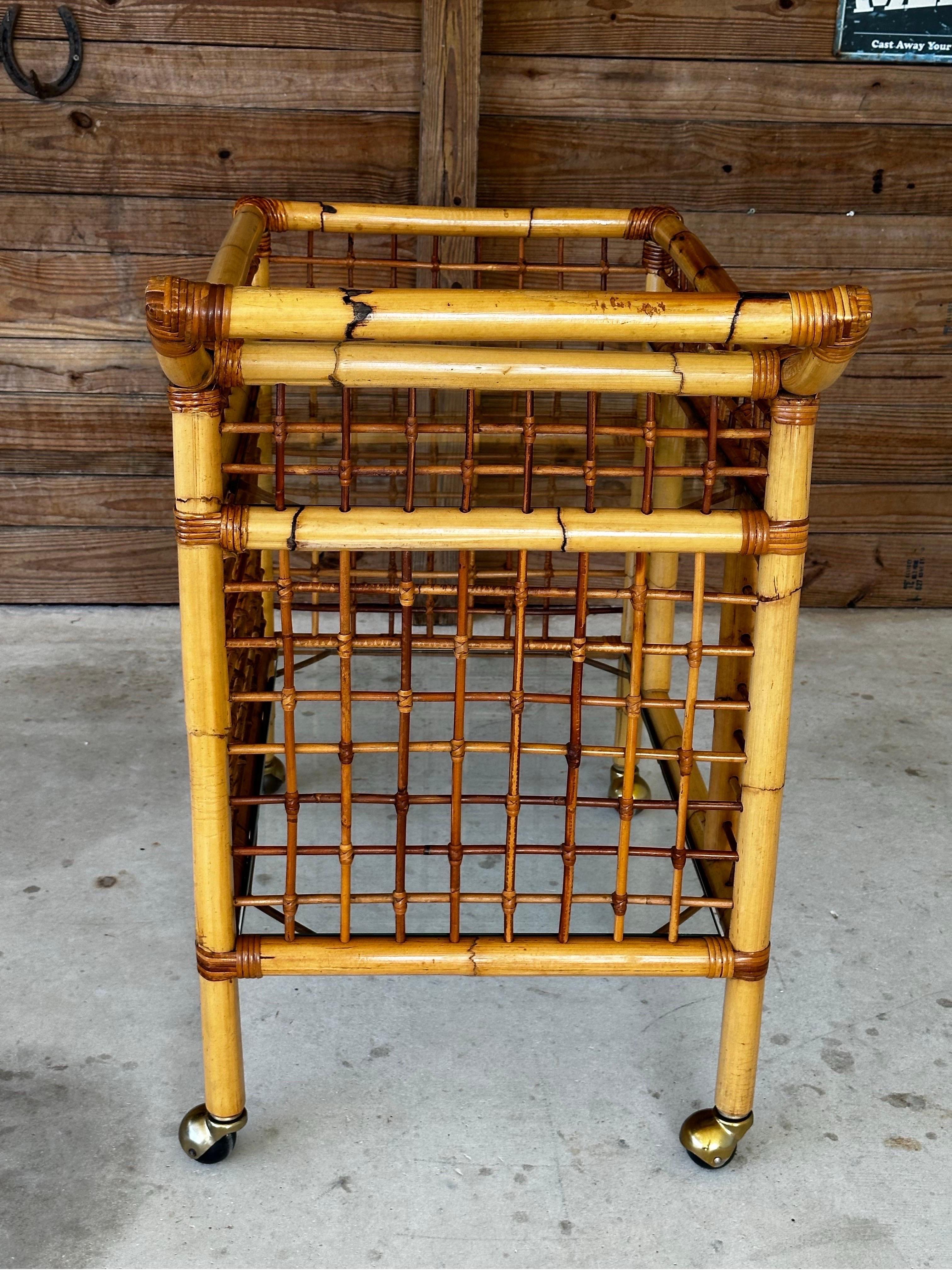 This beautifully refinished and restored vintage 1970s rattan bar cart brings a touch of tropical elegance to your entertaining space. 
Featuring a two-level design, the cart boasts intricate rattan weaving, sturdy construction, and brass-capped