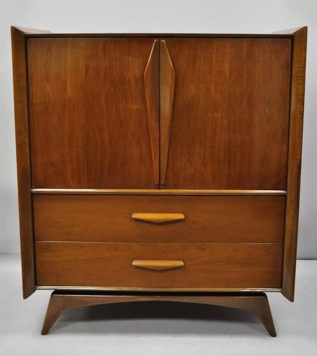 Vintage Mid Century Modern Sculpted Angled Walnut Highboy Tall Chest Dresser. Item features raised panel sculpted wood sides, sculpted wood pulls, angled and tapered legs, two cabinet doors, beautiful wood grain, 5 drawers, sleek sculptural form.