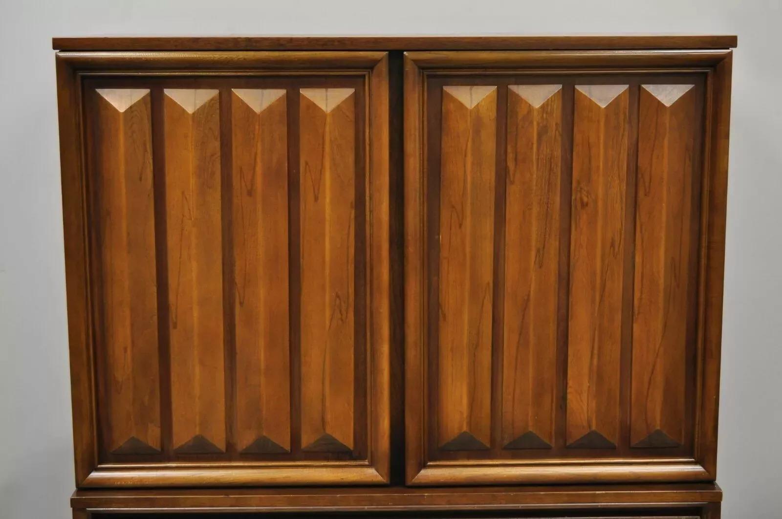 Vintage Mid Century Modern Nussbaum geschnitzt V-Leg Tall Chest Dresser Cabinet. Das Möbelstück zeichnet sich durch spitz zulaufende, V-förmige Beine, geschnitzte Türverkleidungen, schöne Holzmaserung, 2 Flügeltüren, 8 eingezinkte Schubladen,